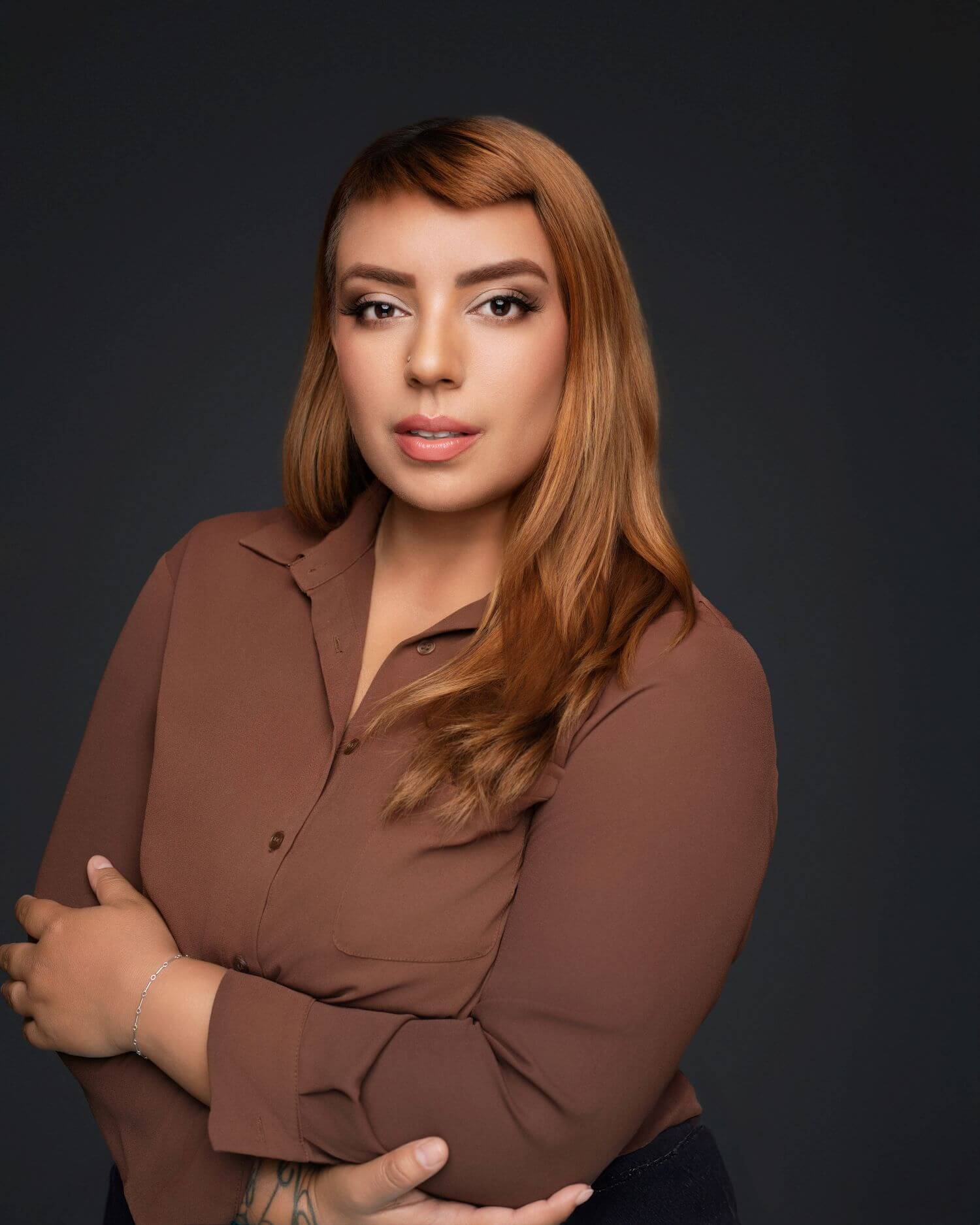 Brunette woman standing in professional brown top with makeup done by OKOS Creations.