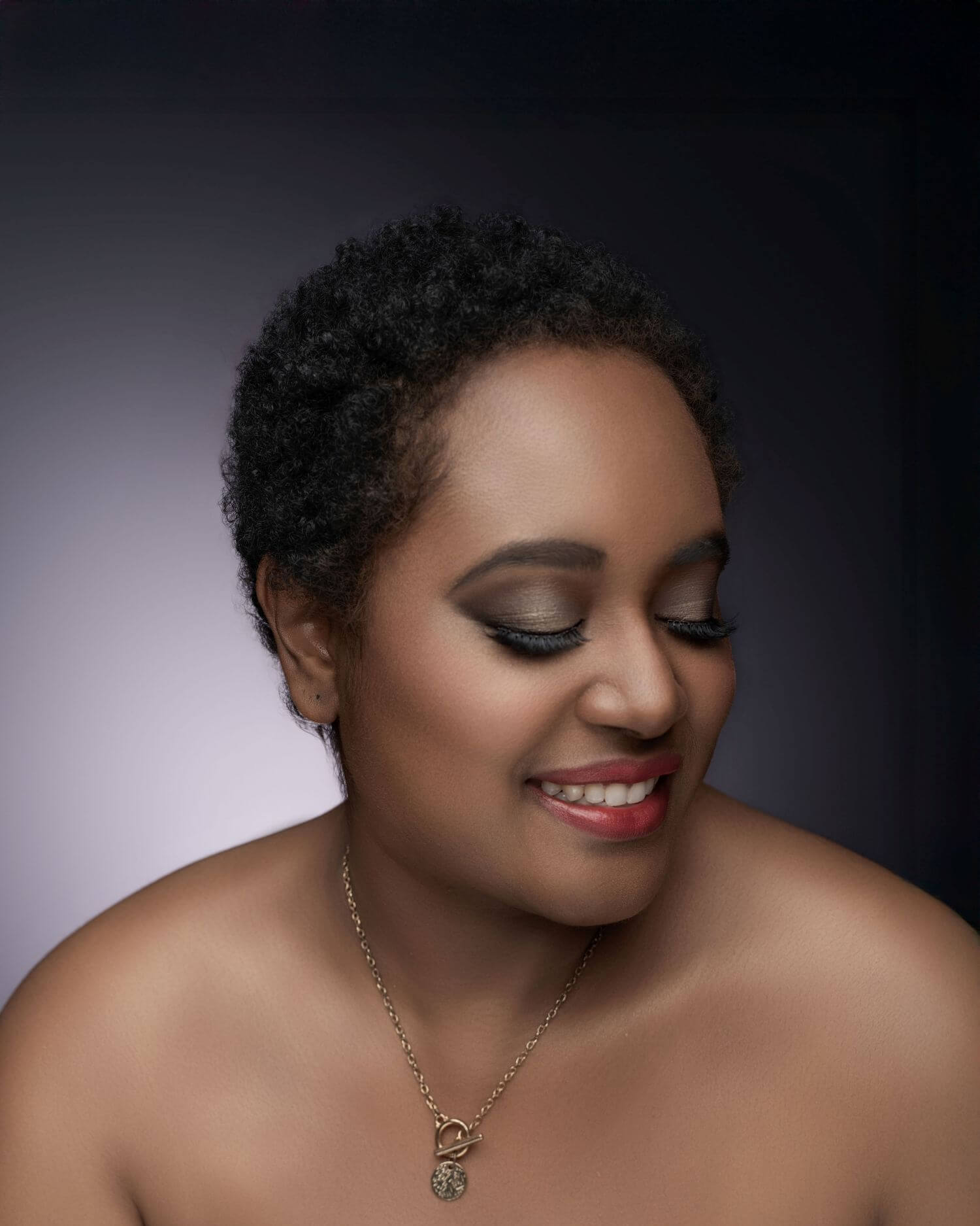 Woman looking down, smiling in beautiful makeup by OKOS Creations.