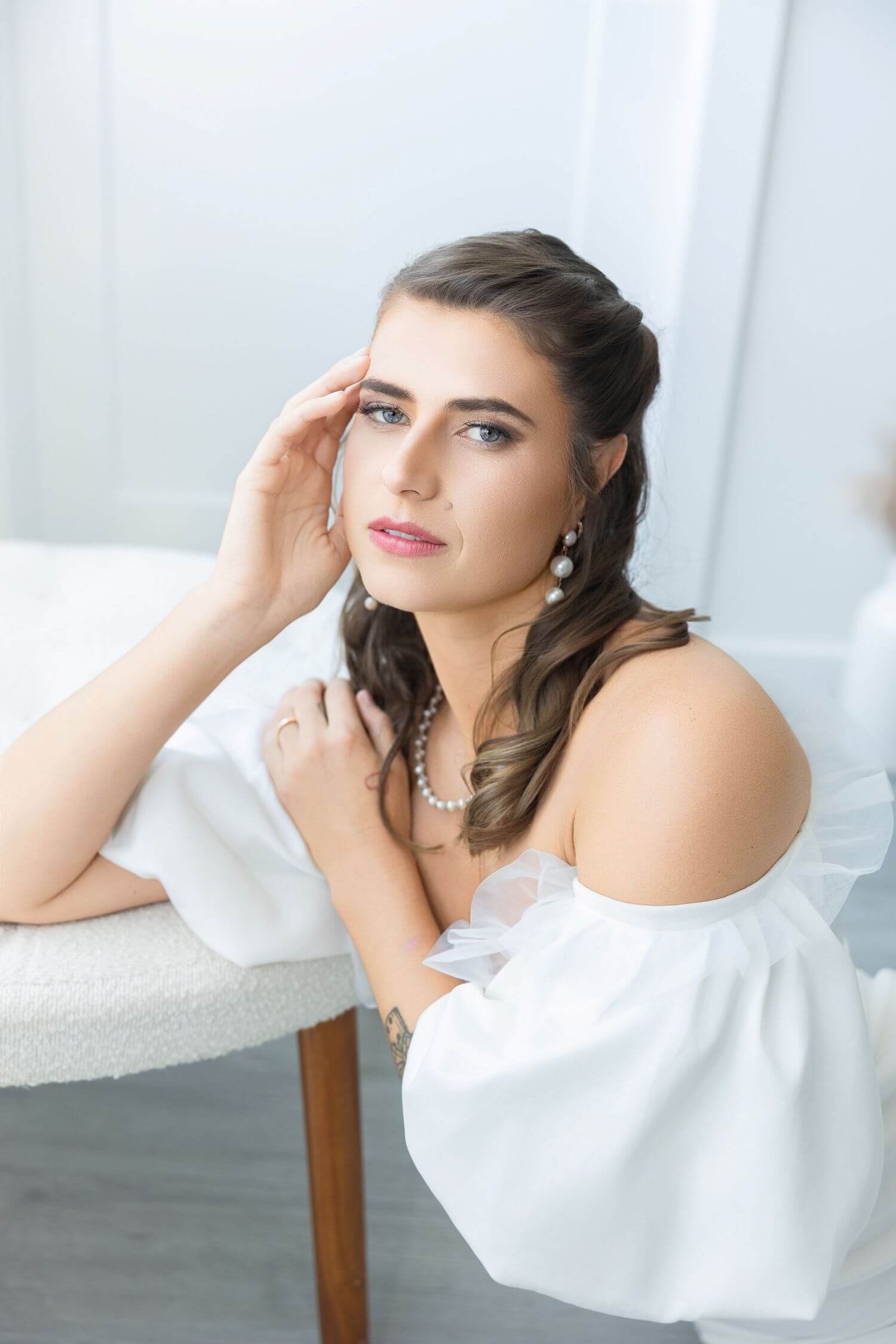 Young bride in timeless makeup, head resting on hand, elbow on table.
