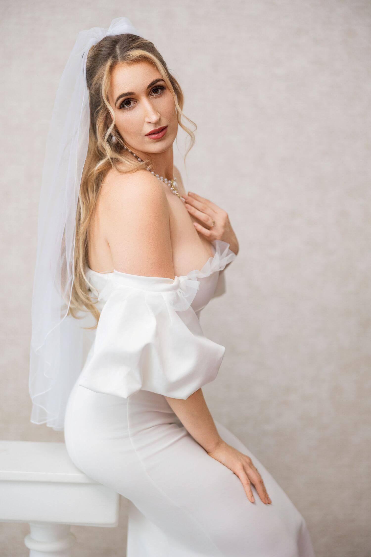 Blonde bride sitting on white bench, natural beauty makeup done by OKOS Creations.