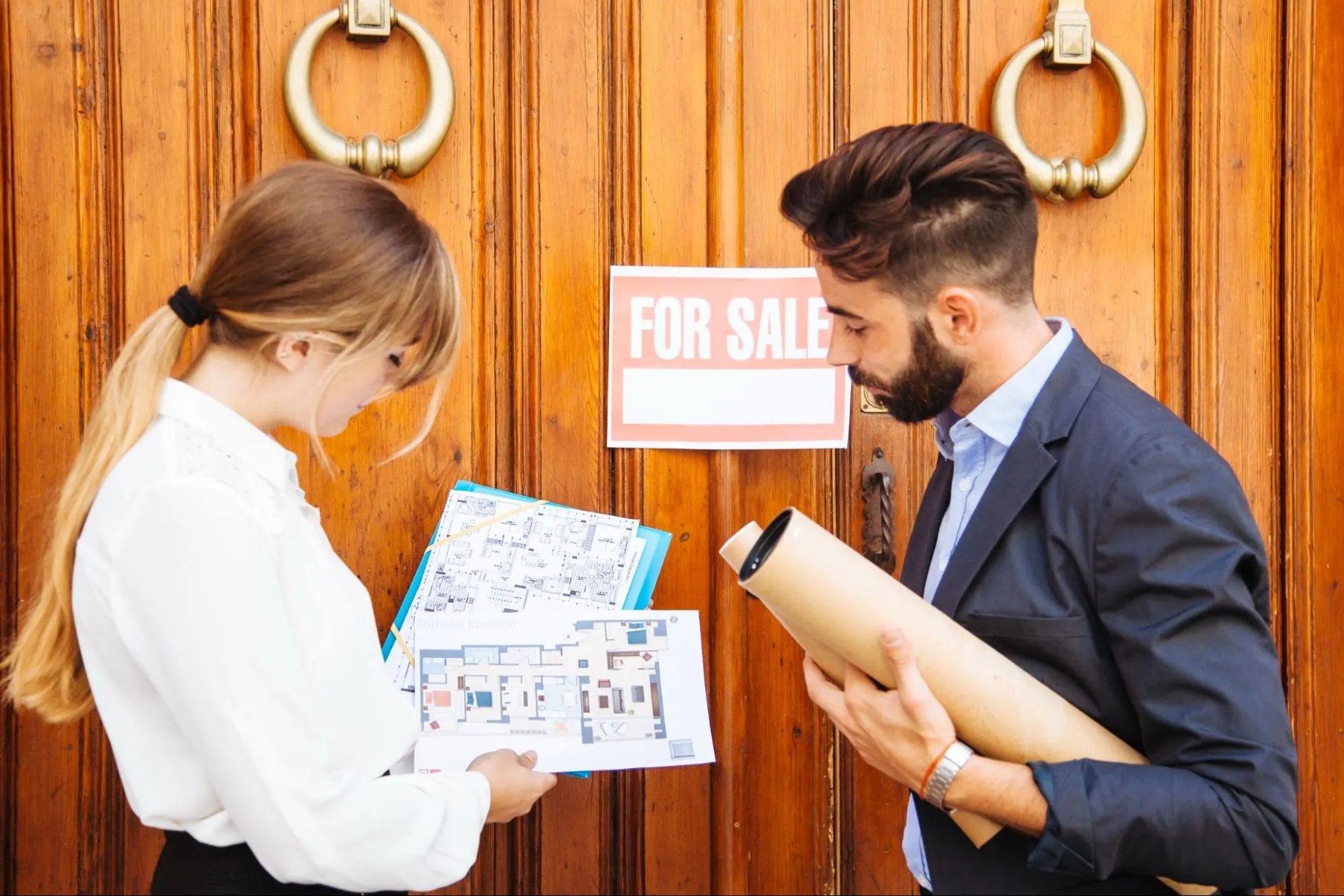 Real estate agents waiting outside a house for sale with plans and paperwork in hand.