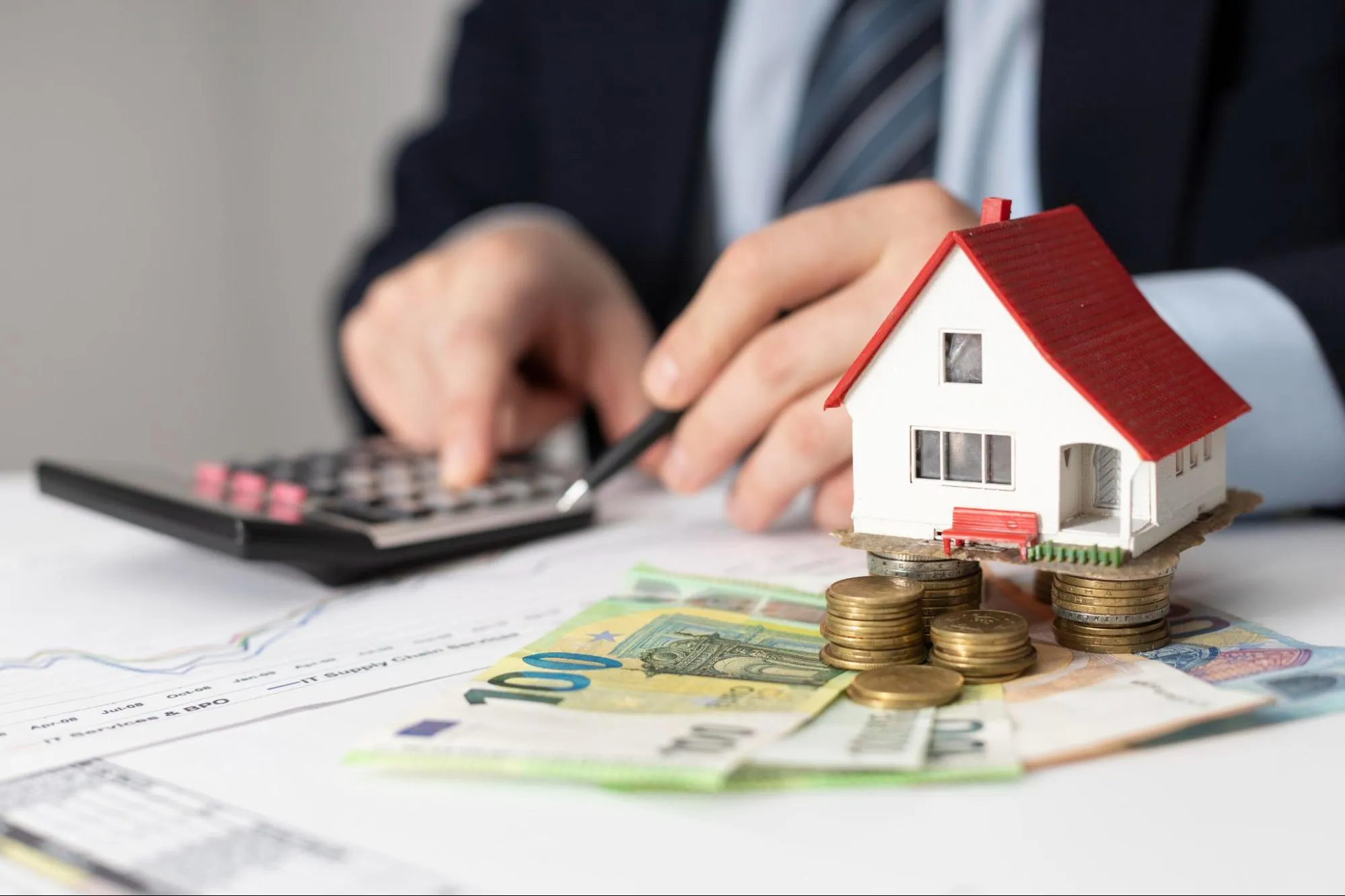 Person using a calculator with cash and miniature house on the table.