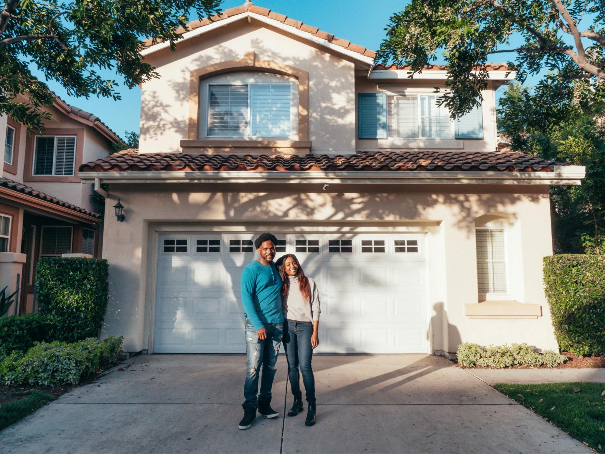 A couple standing happily outside a newly bought house.
