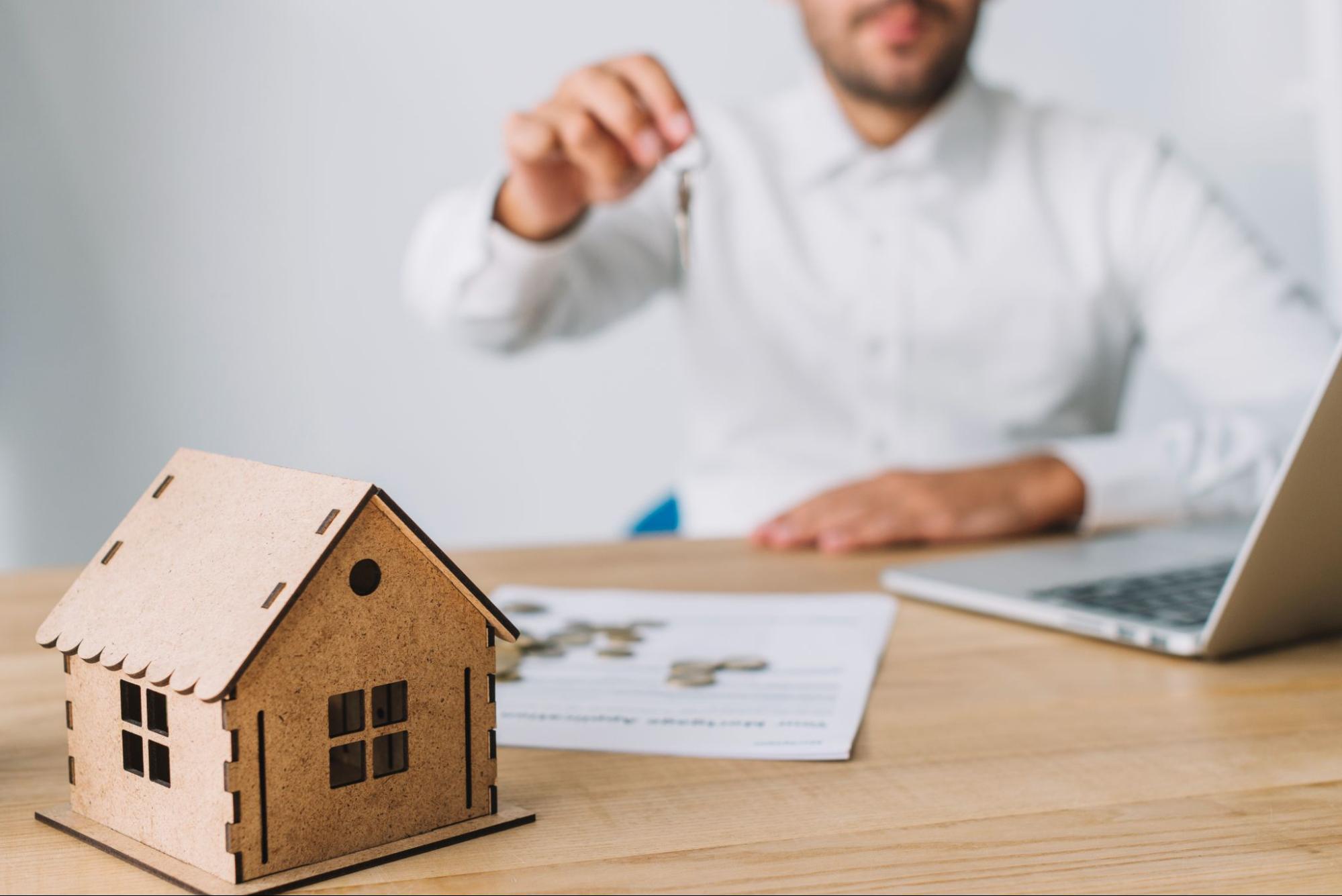 A miniature house and a real estate agent holding a key.