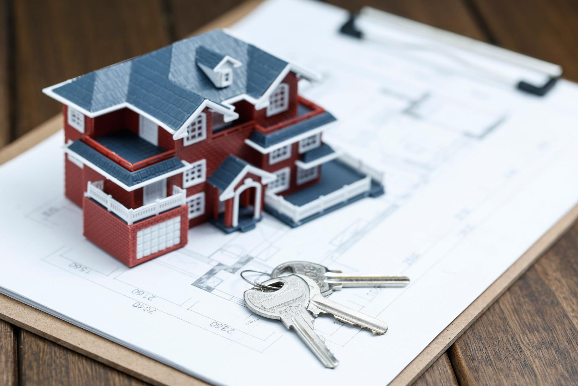 A miniature house with construction plans and keys on the table.