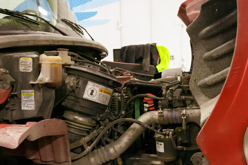 Air inlet manifold inspection on a red semi truck engine bay with WARNING and CAUTION labels.