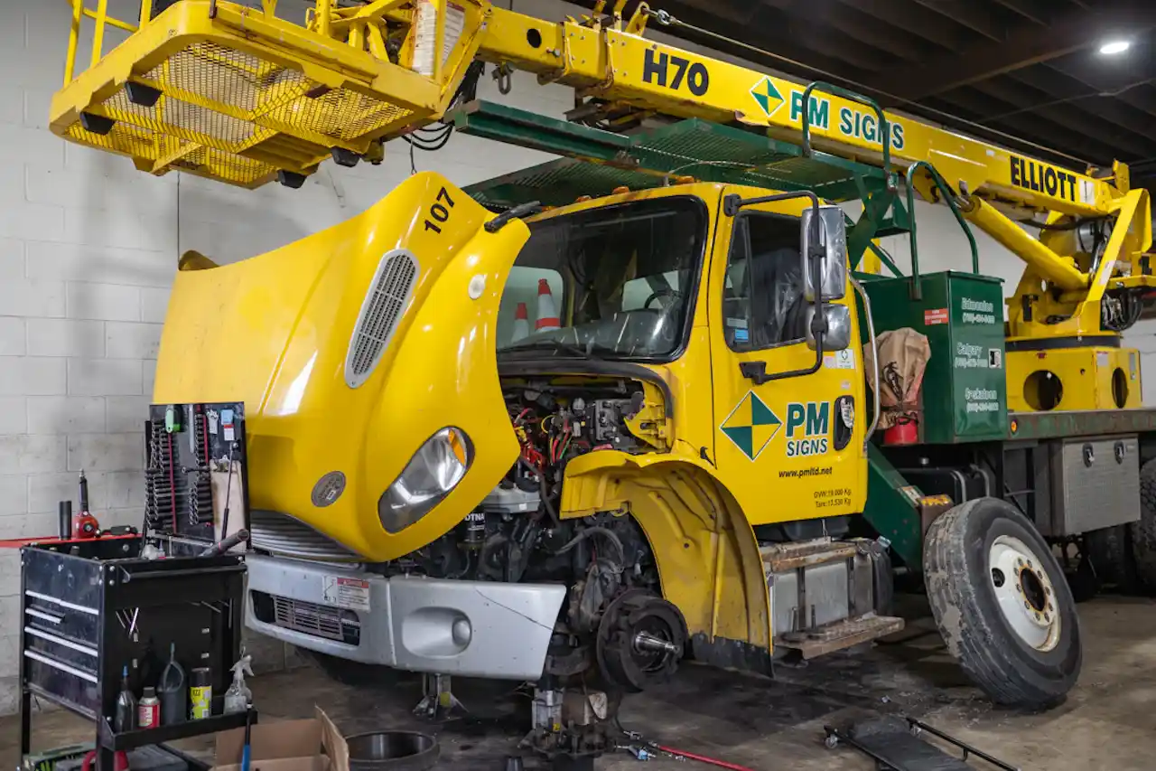 Dielectric testing service for a heavy-duty bucket truck, shown in a repair shop with its hood open and wheel removed.