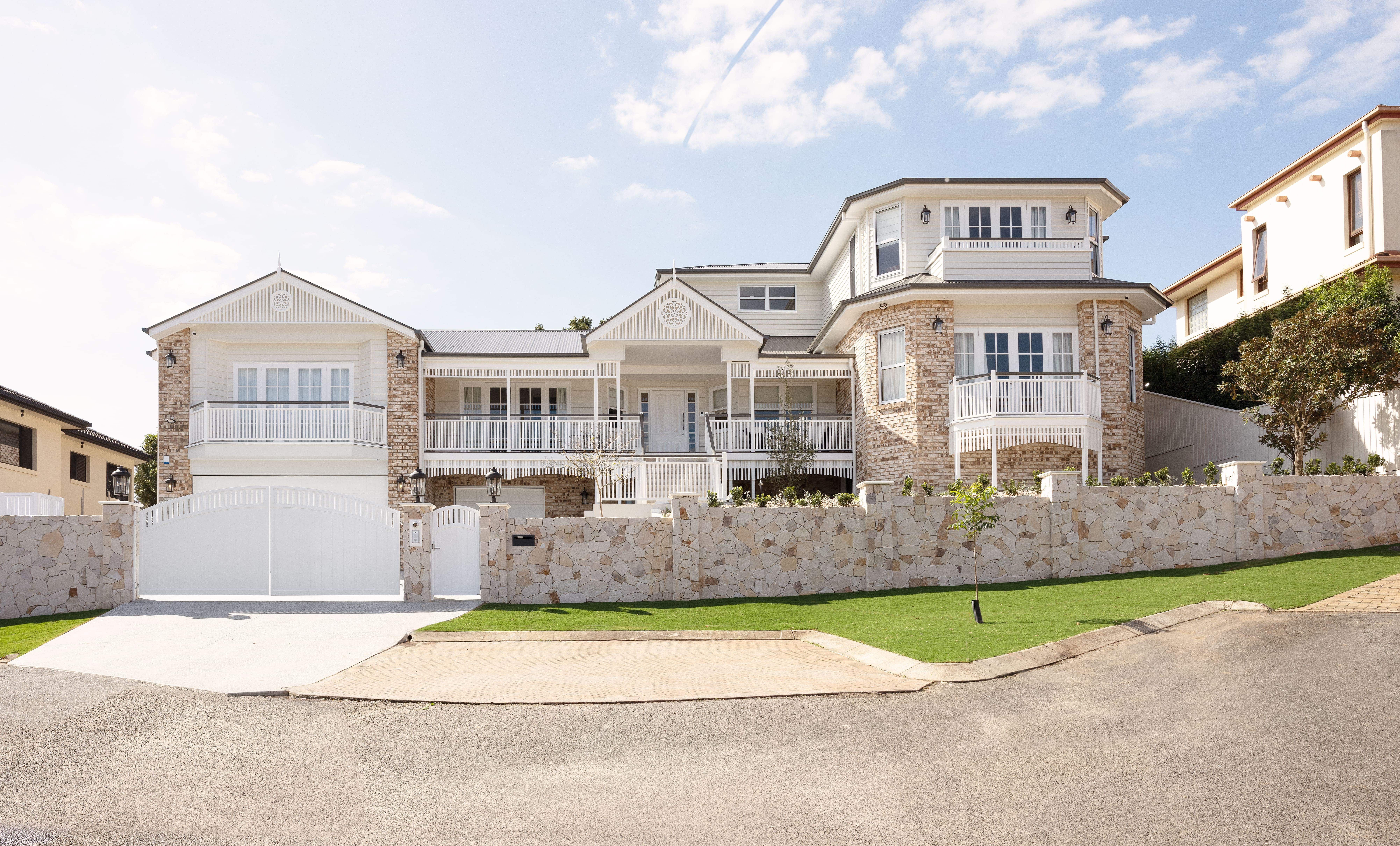 Full front facade from the street, including stone wall and white gates.