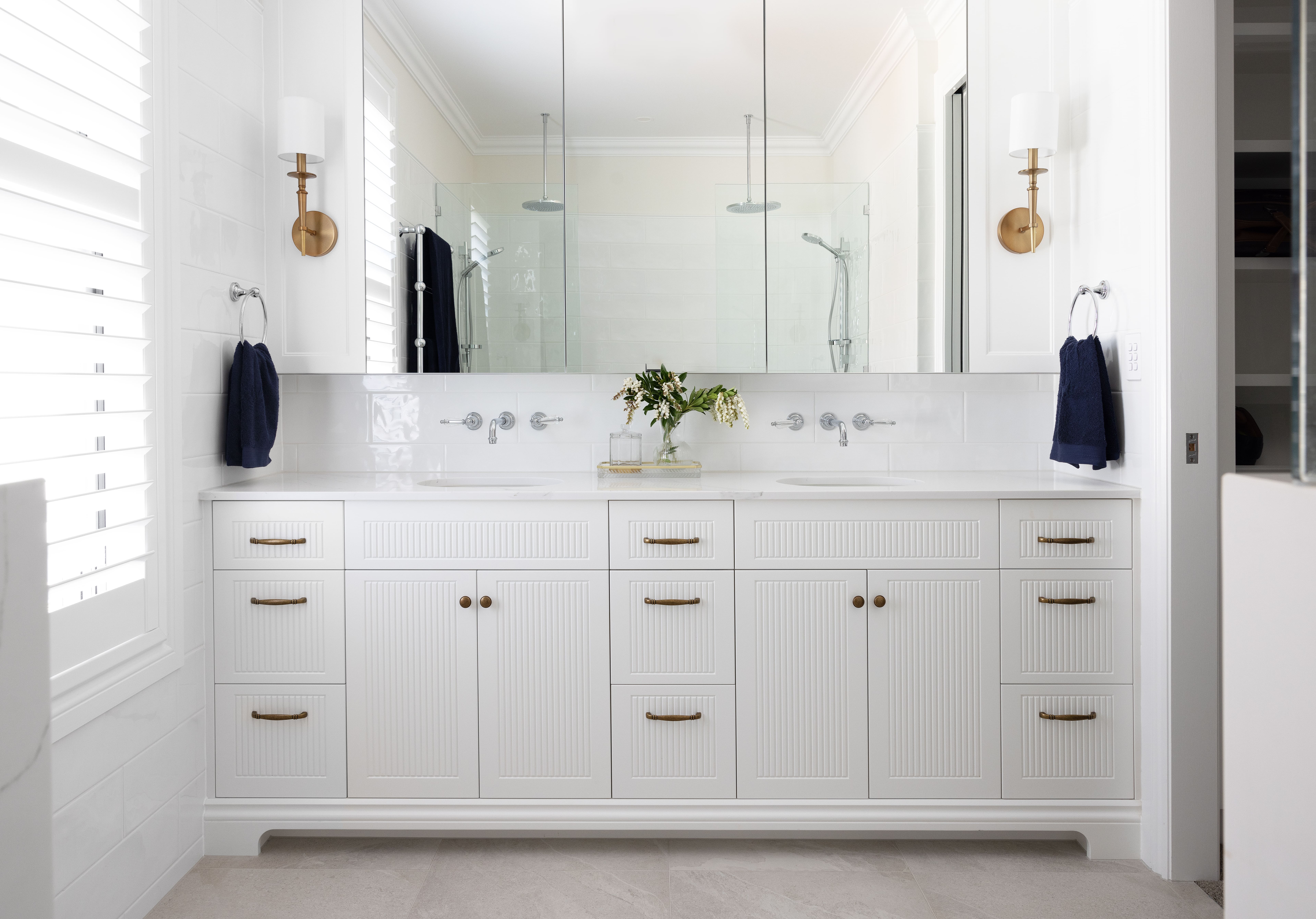Ensuite vanity with mirrored cabinets, detailed cabinetry, and brass and white lighting on the side of the cabinetry