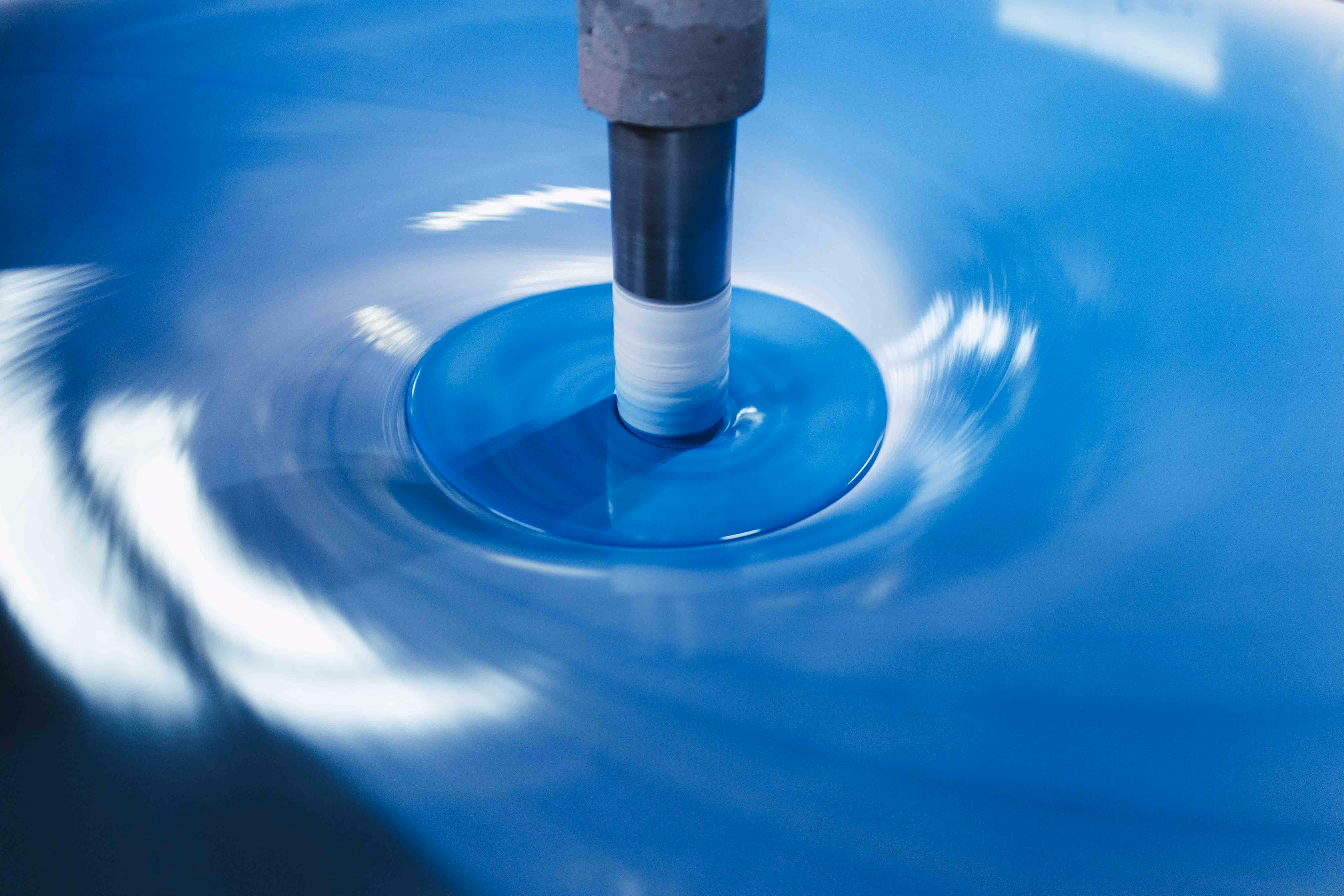 Eine Nahaufnahme eines rotierenden Maschinenbauteils, das in einer blauen Flüssigkeit läuft.