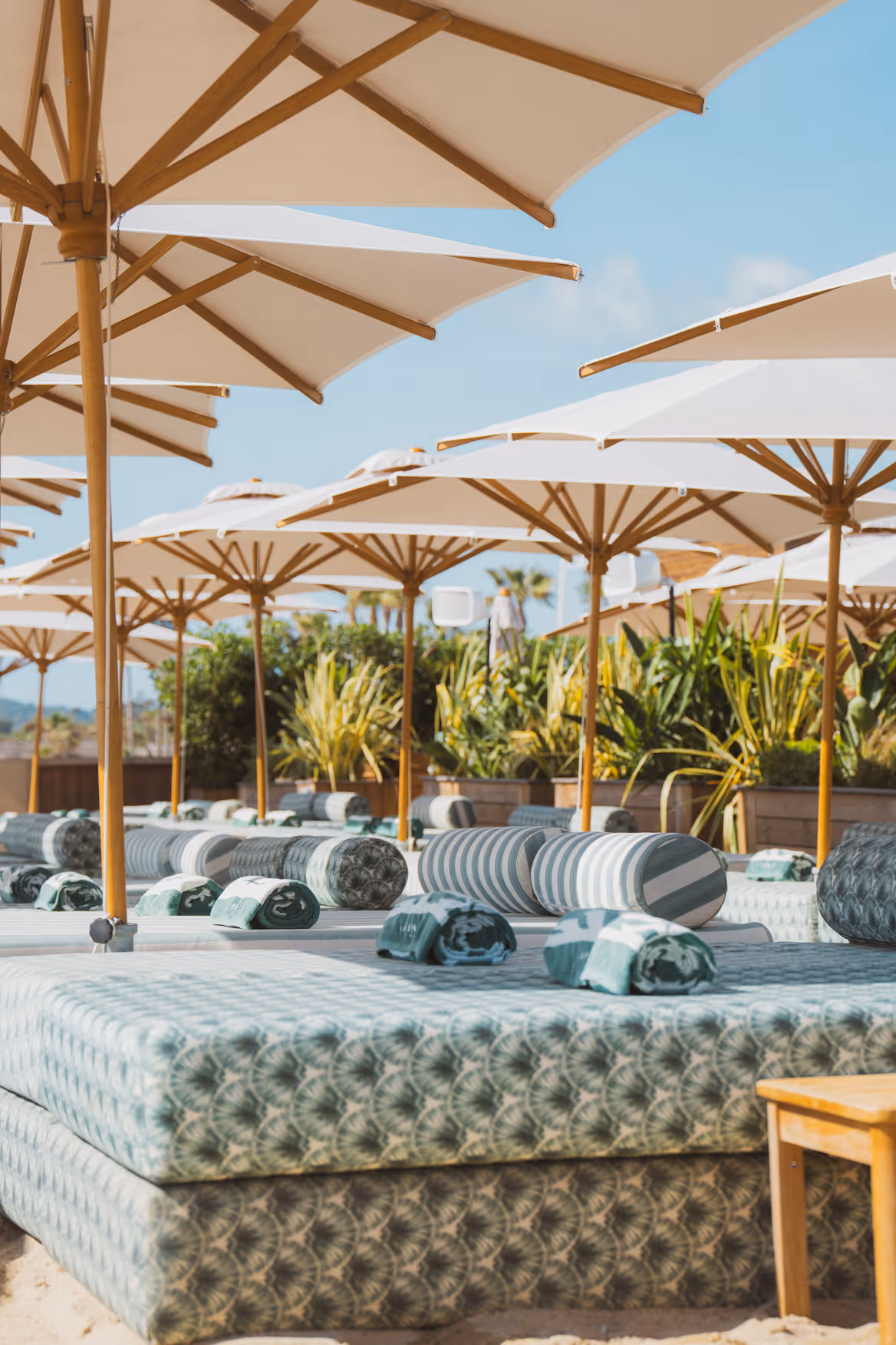 Lits de plage confortables avec coussins rayés sous de grands parasols blancs sur une plage ensoleillée.