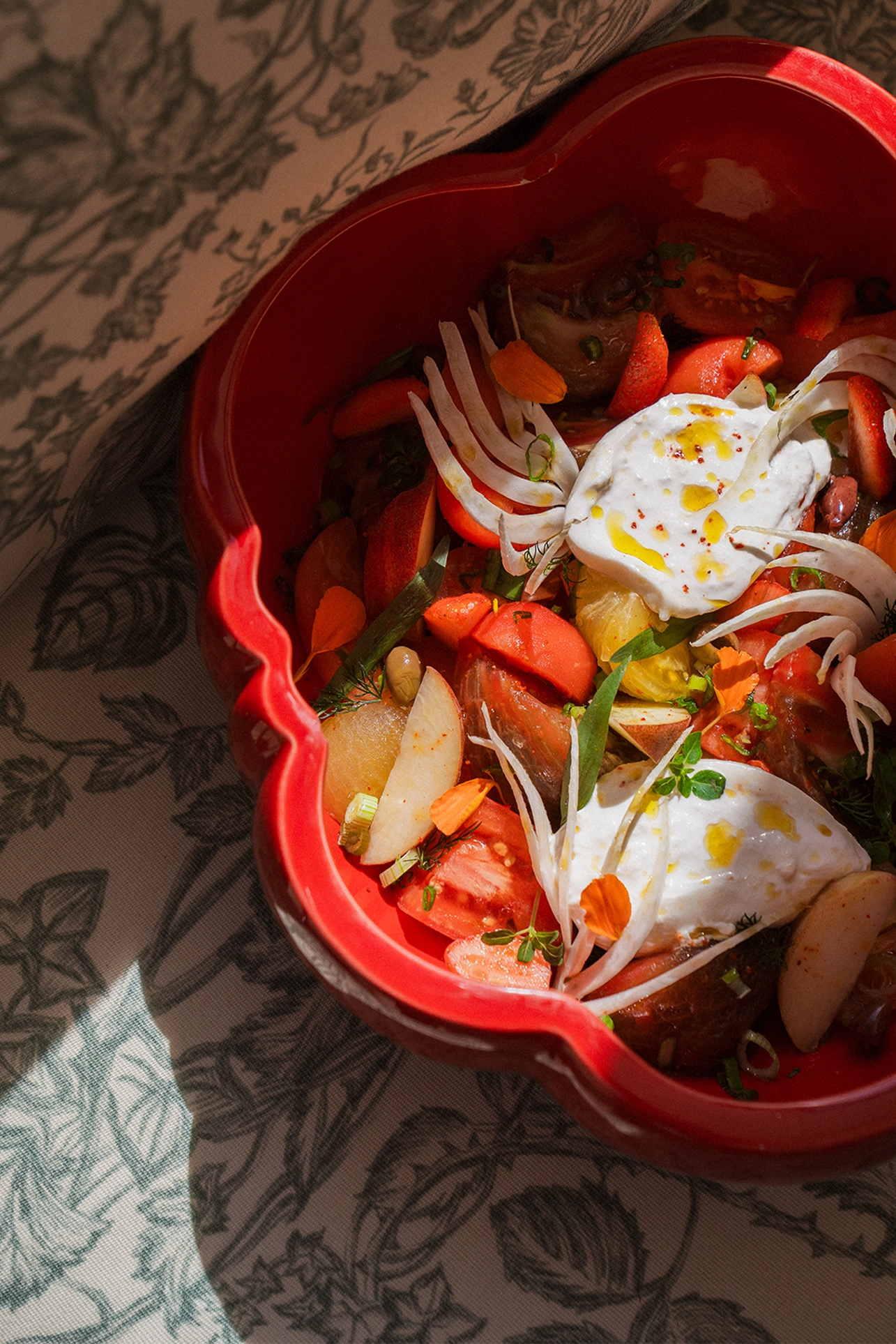 Salade colorée avec tomates, fines tranches de pommes, herbes fraîches, morceaux de fenouil et deux quenelles de fromage blanc dans un bol rouge.