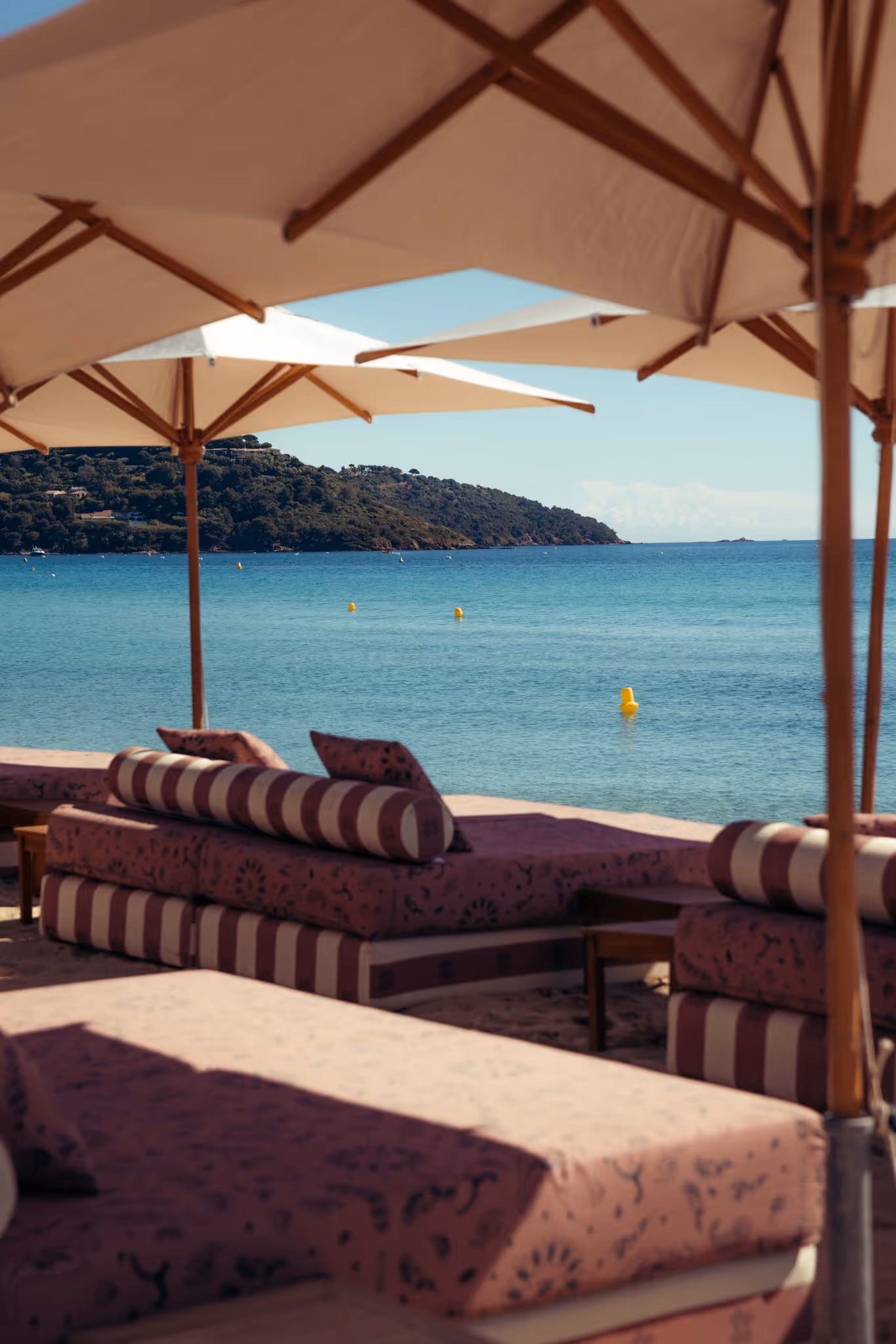 Chaises longues rayées et ombrelles sur une plage avec vue sur mer et colline verte.