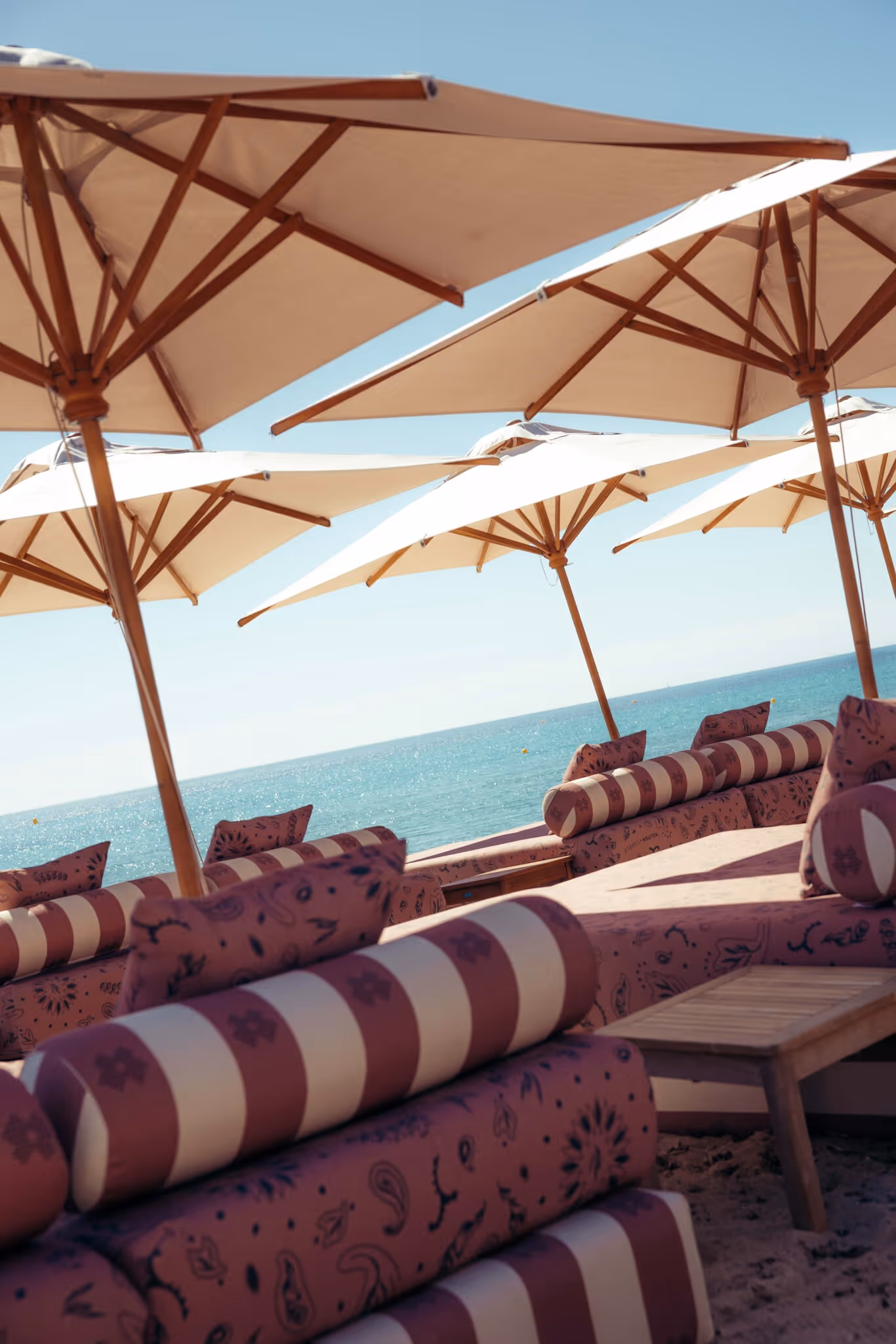 Chaises longues rayées et parasols blancs sur une plage avec vue sur l'océan.