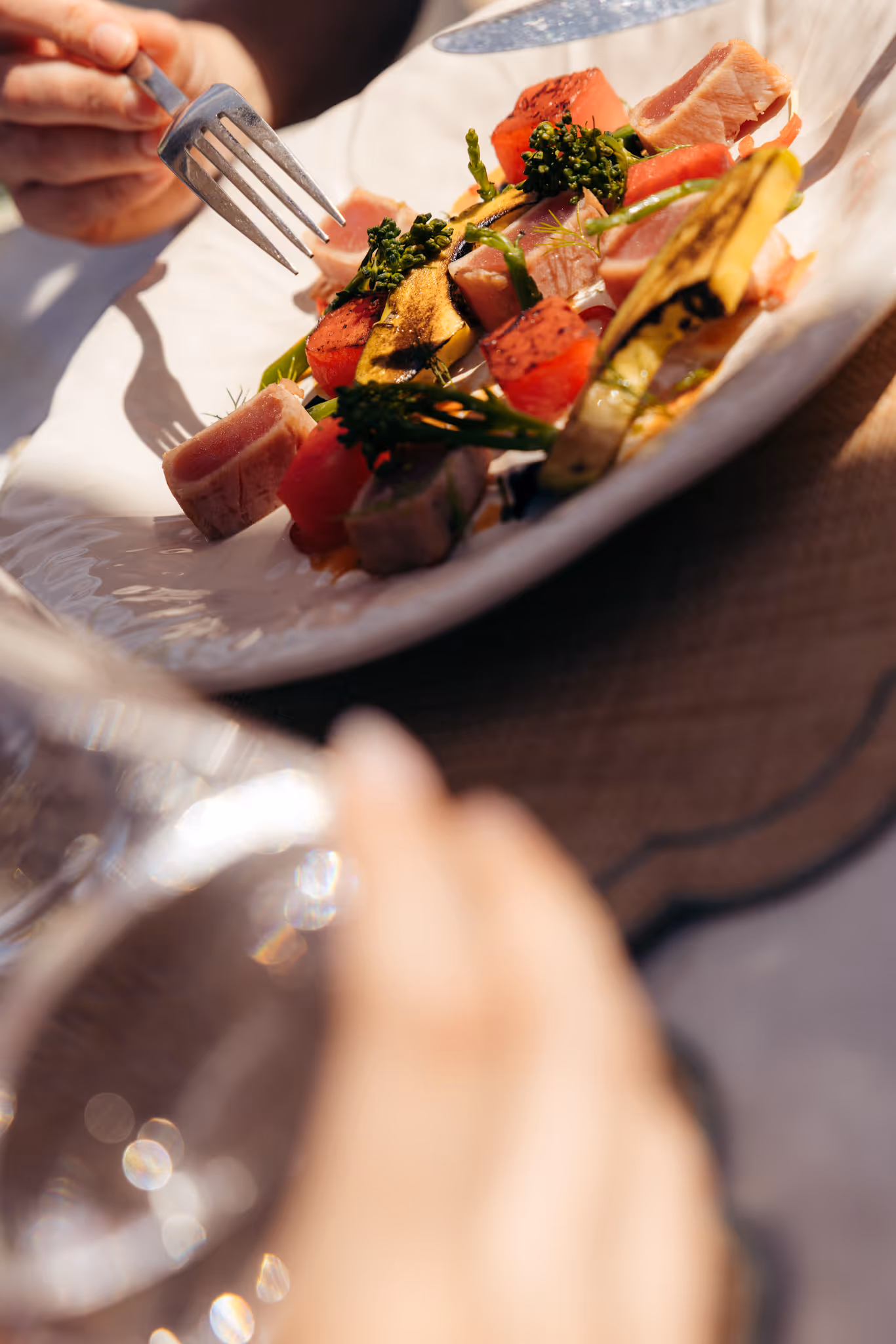 Person mangeant un plat avec morceaux de poisson, légumes grillés et brocoli sur une assiette blanche.