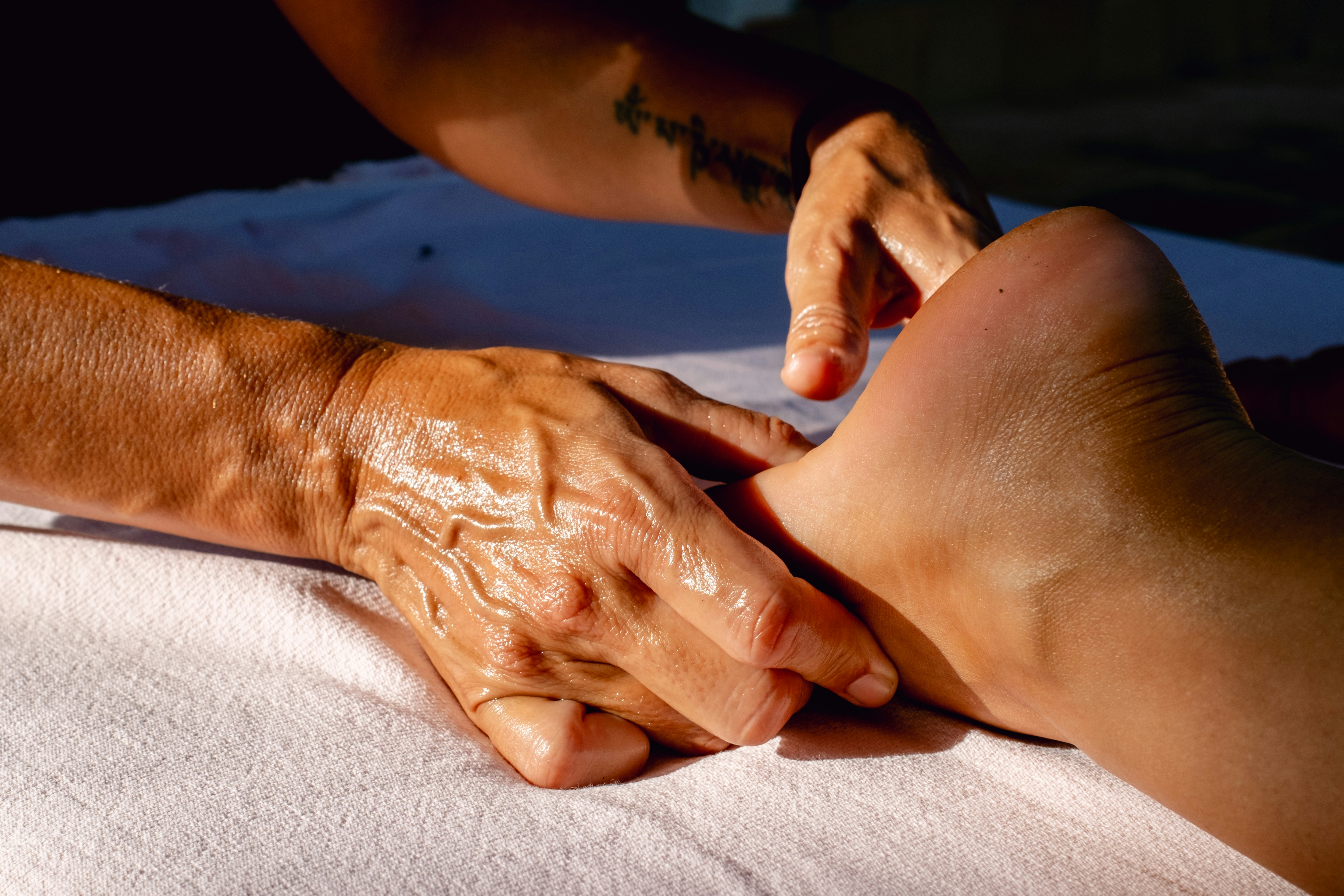 The image shows a close-up of a person receiving a foot massage, with the masseur applying oil and pressure to the foot. The main themes are relaxation, therapeutic touch, and wellness practices aimed at foot care and stress relief.