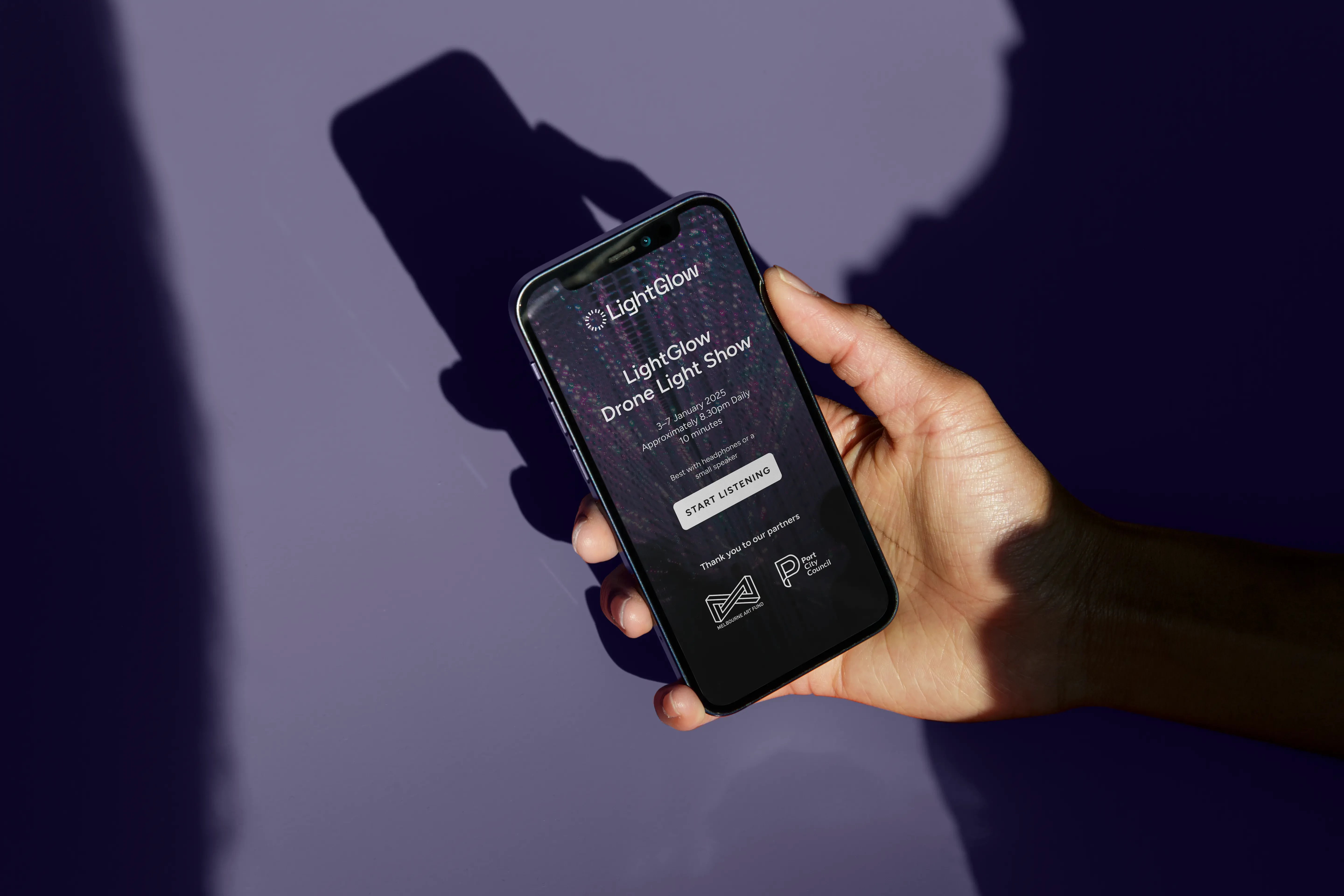 A hand holds a smartphone displaying an Event Sync audio guide for the “LightGlow Festival Drone Light Show”, with a purple background and screen showing show details, a Start Listening button, and partner logos.