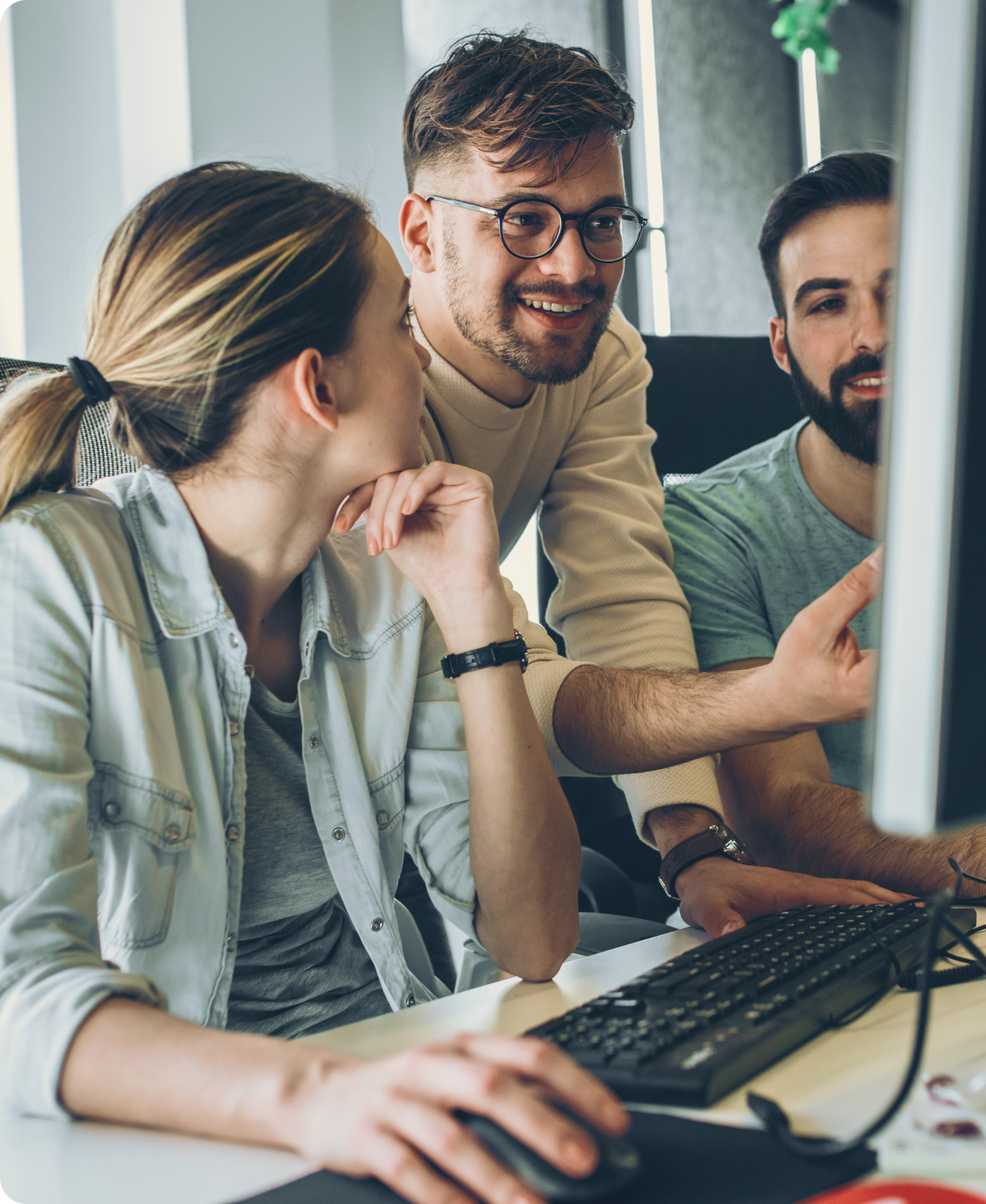 Three young colleagues collaborating and looking at a computer screen in an office.