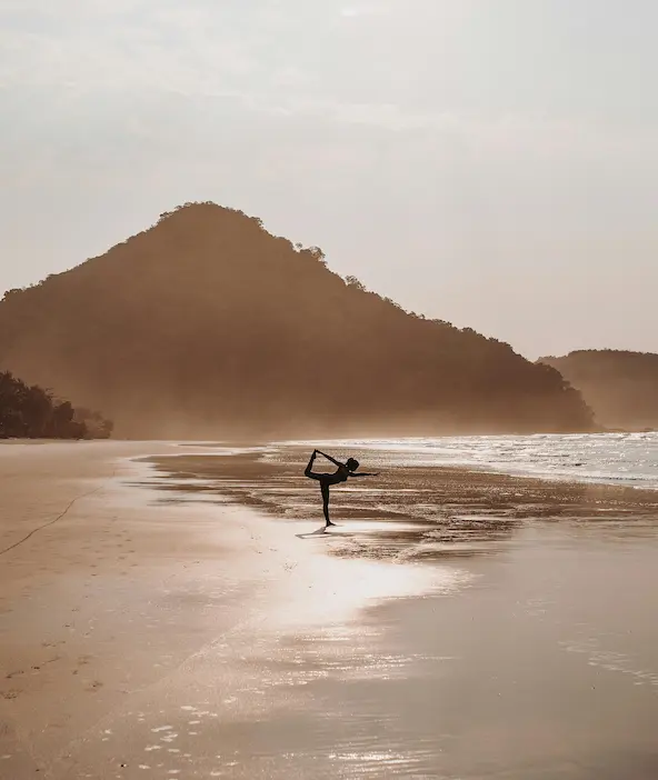Une femme réalisant une séance de yoga sur la plage.