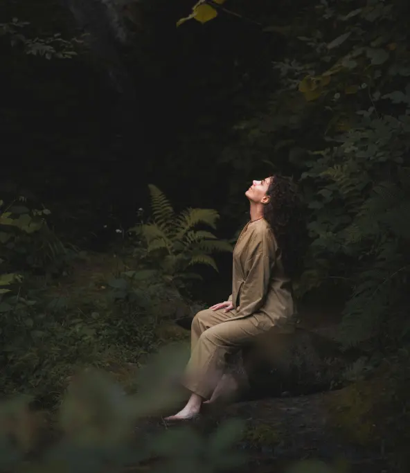 Femme en harmonie avec la nature, entourée d’arbres dans une forêt tranquille.