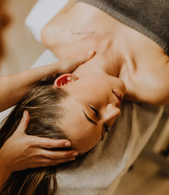Femme allongée recevant un massage relaxant du cou dans un cadre apaisant.