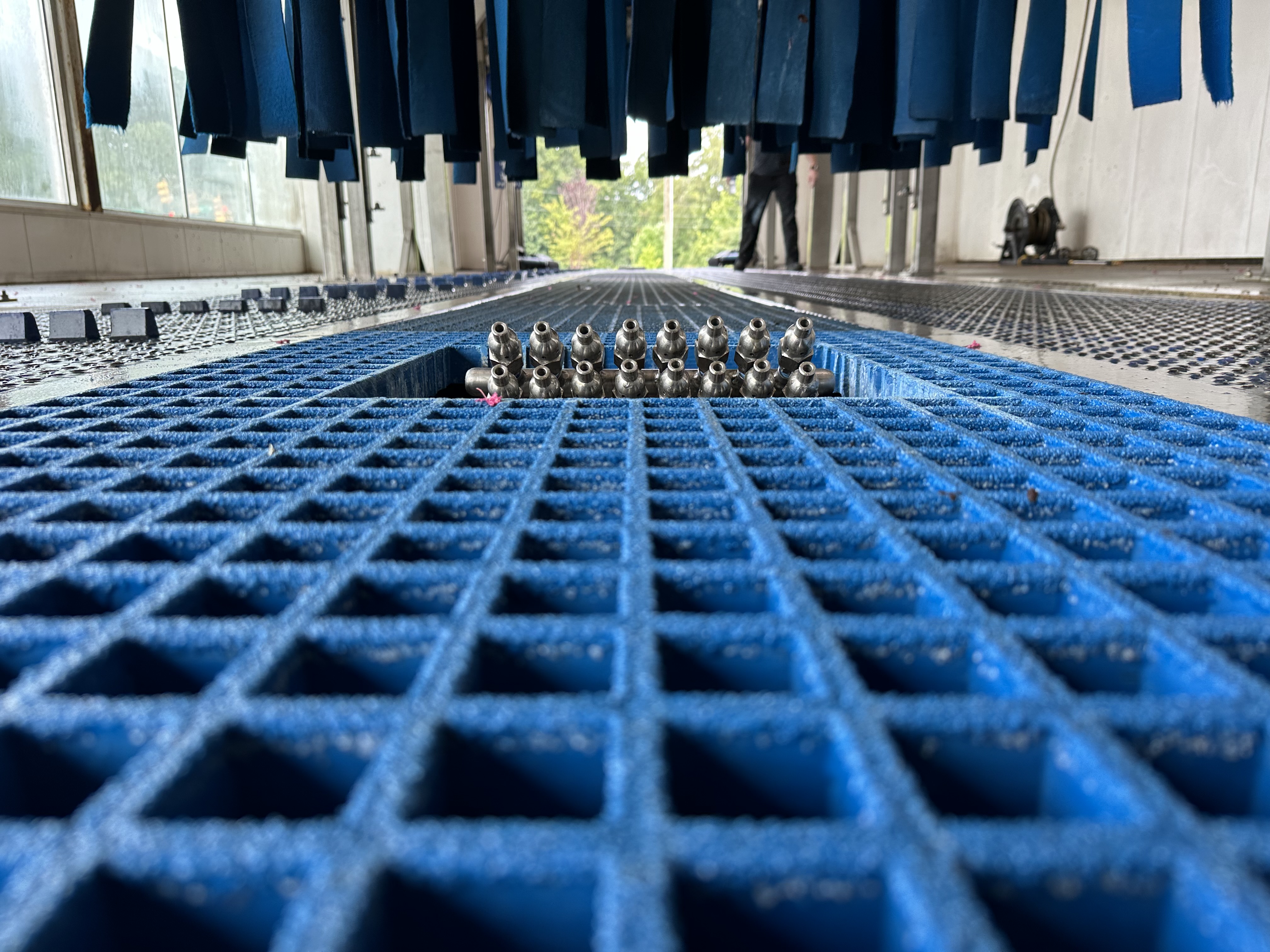 Close-up view of blue grated floor surface with metal nozzles and hanging blue brushes in a car wash. car wash equipment to clean bumpers with high pressure.