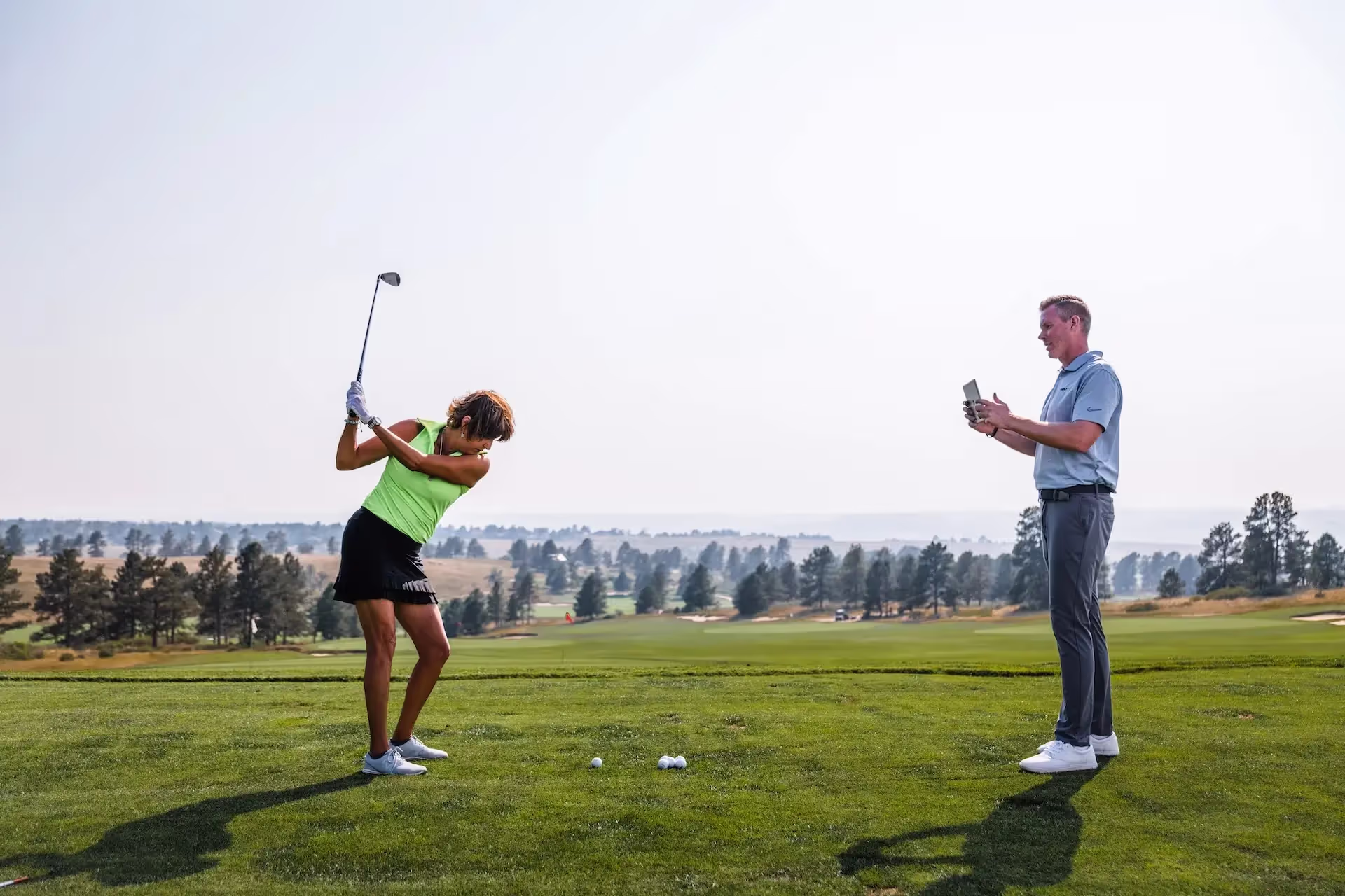 Woman being filmed on driving range by GOLFTEC coach to improve swing