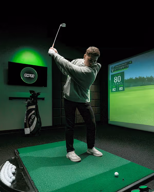 Golfer in GOLFTEC hitting bay in back swing ready to hit the ball into the simulator screen 