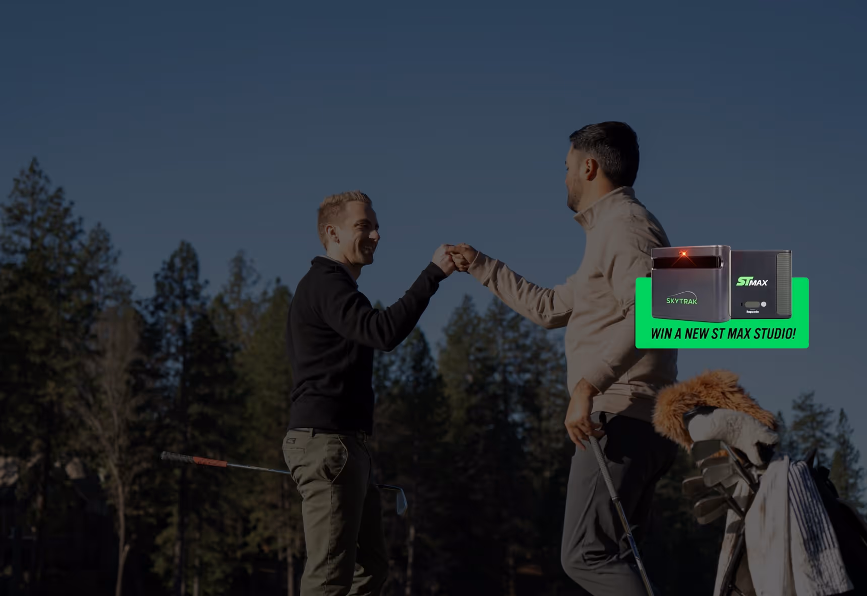 Two golfers fist bump on a golf course with clubs and golf bags nearby under a clear blue sky.
