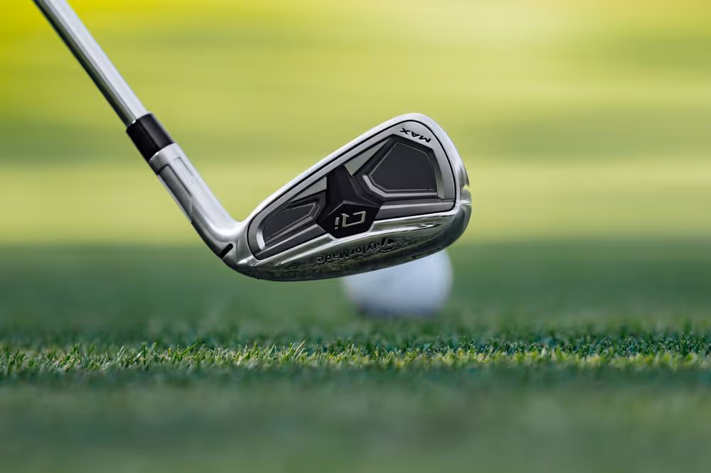 Close-up of a TaylorMade golf iron preparing to strike a golf ball on the grass.