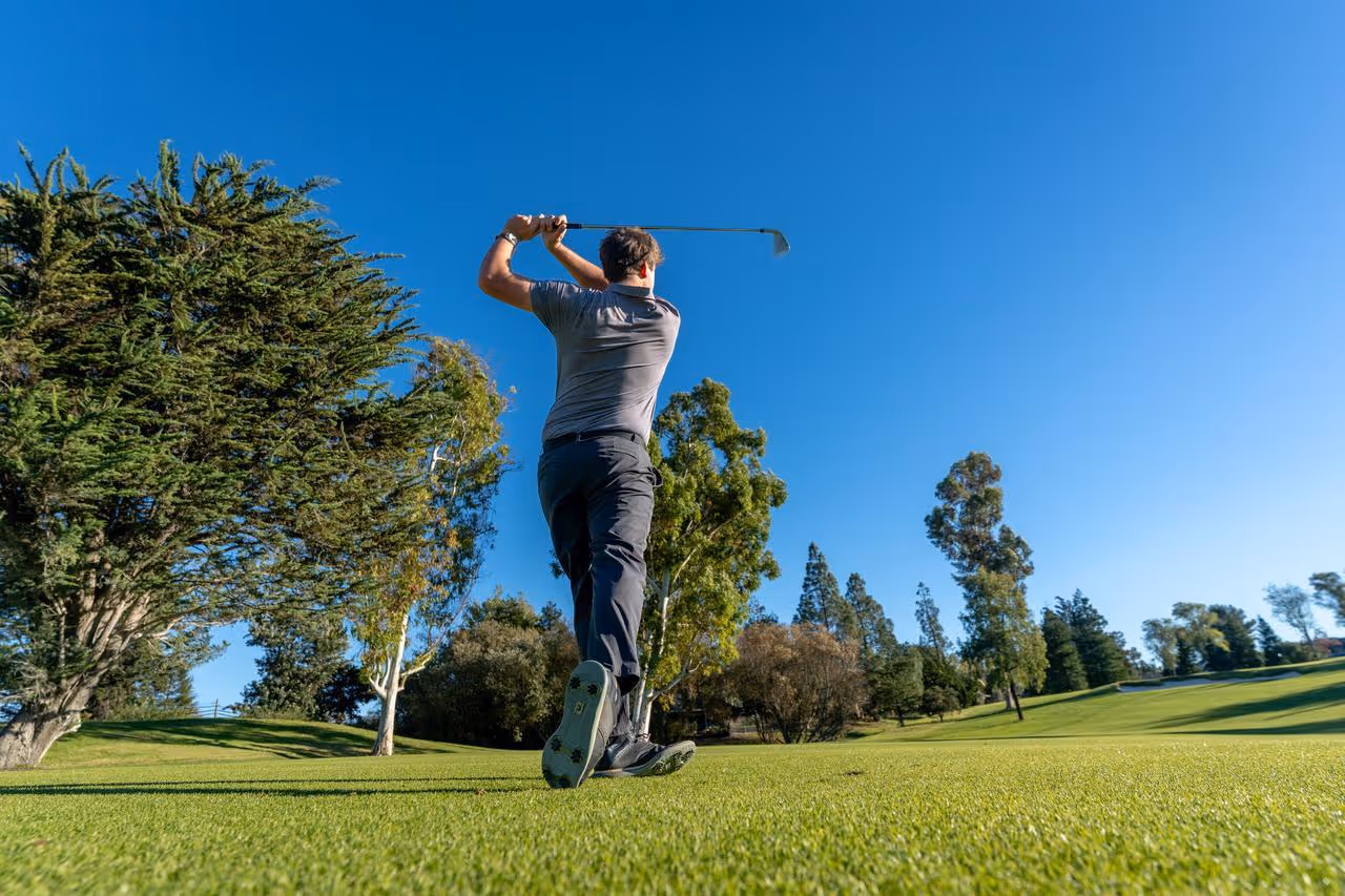 Golfer finishing a swing on a green golf course under a clear blue sky.