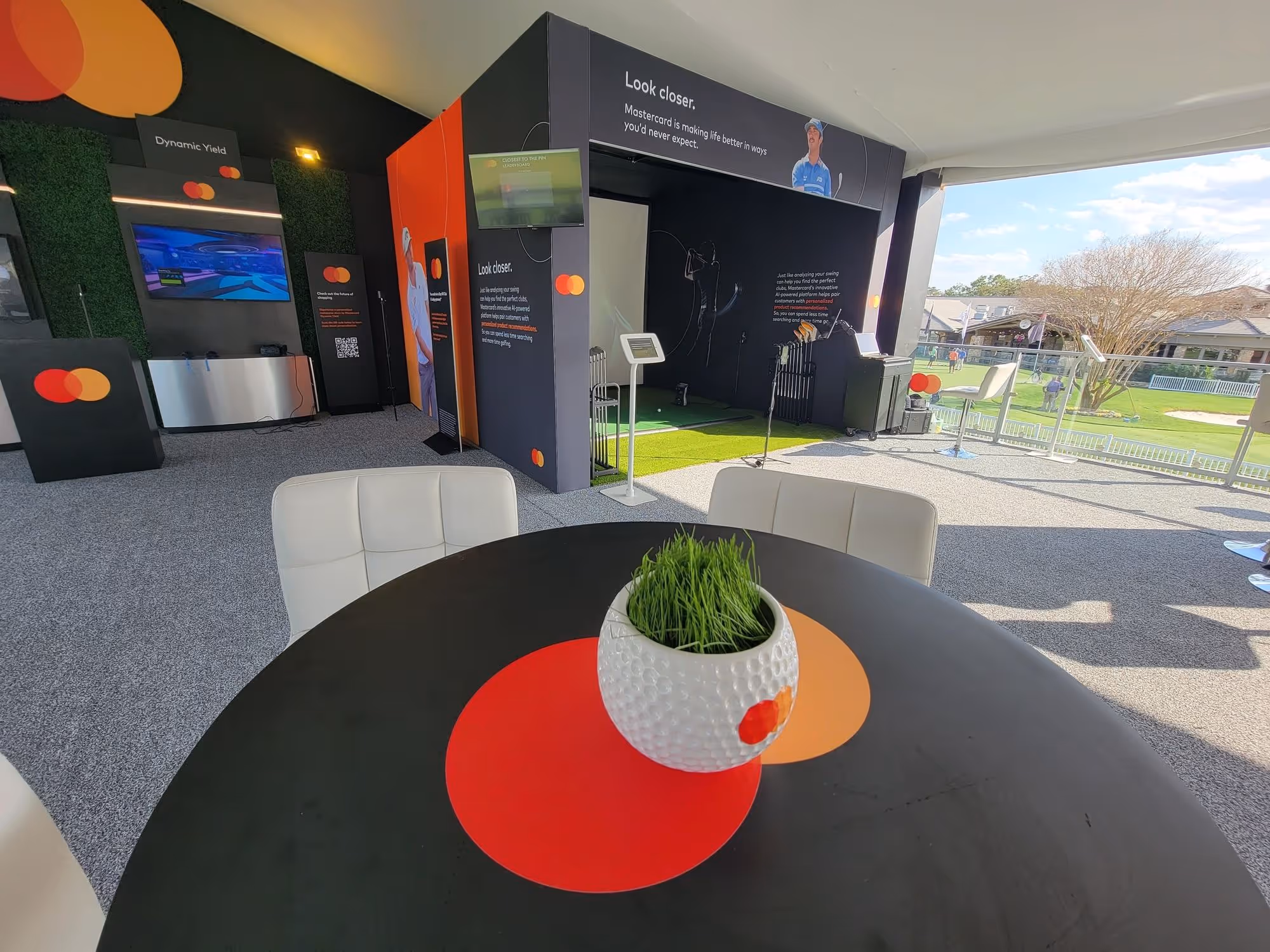 Indoor golf simulator area with Mastercard branding and a round table with a golf ball-shaped planter in the foreground.