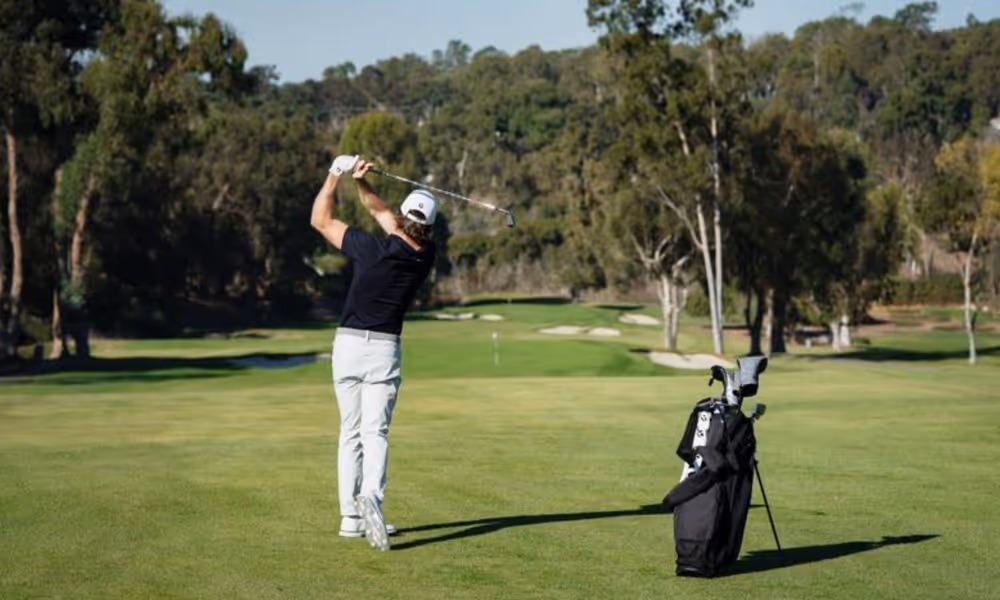 golfer in backswing using an iron on the fairway hole in the distance