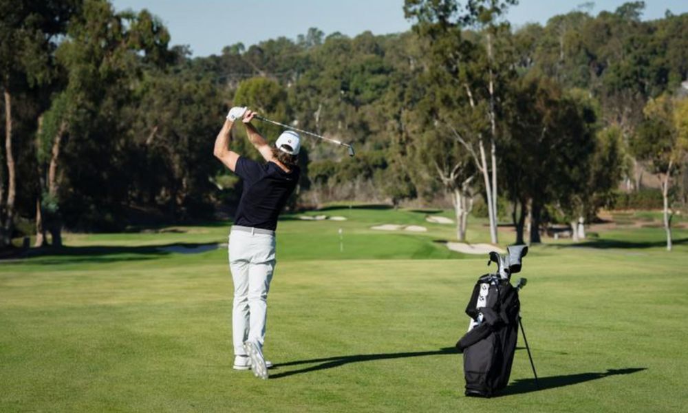 golfer in backswing using an iron on the fairway hole in the distance