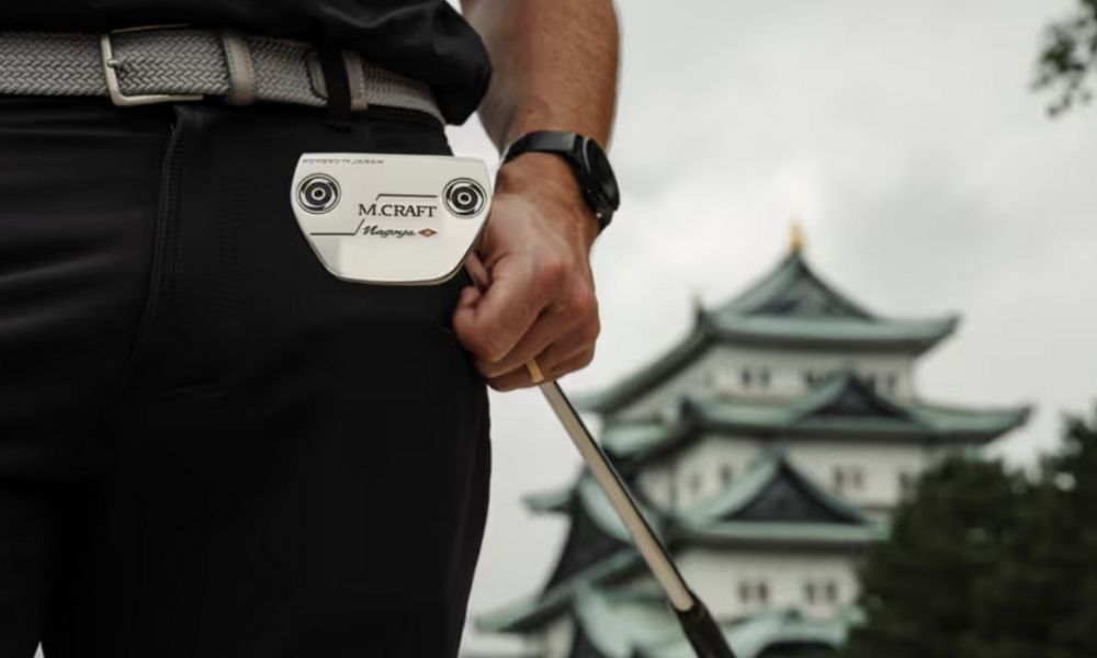 Golfer holding a Mizuno M-Craft putter with Japanese-style building in background