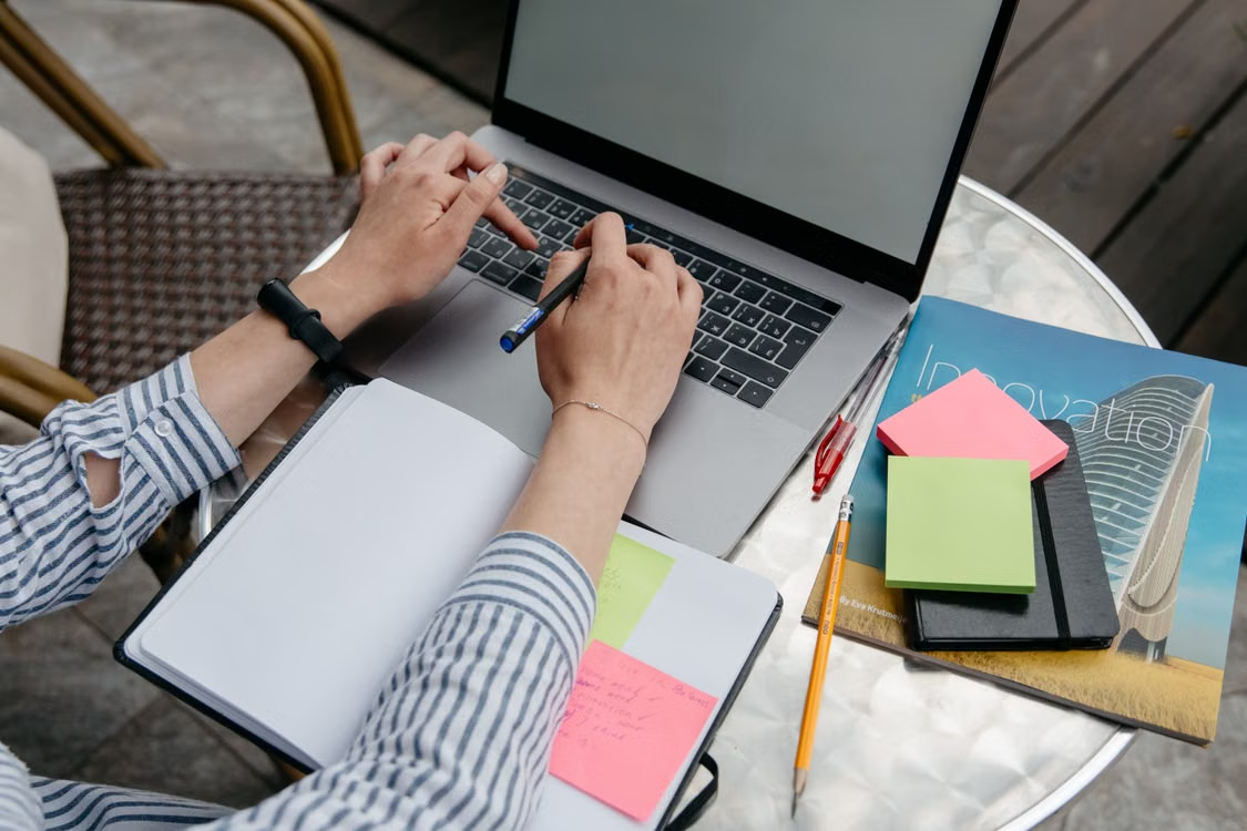 A middle-aged author's hands taking notes beside a laptop and open notebook