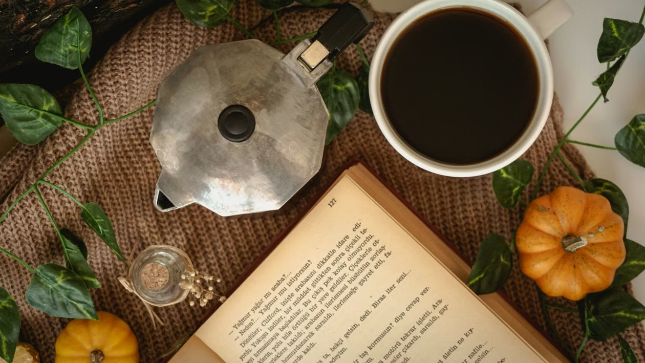 : Close-up flat lay of a hardcover book surrounded by candles, coffee, and autumn-toned props