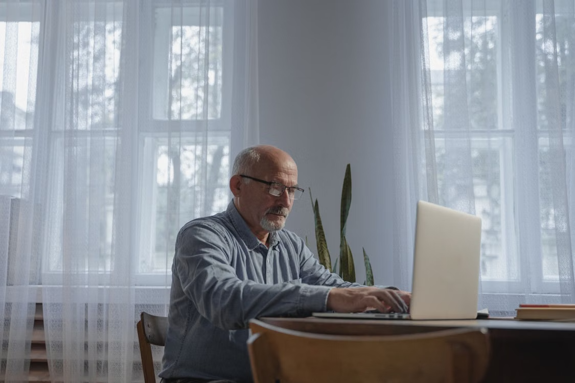 A man in his 60s at a desk, typing on a laptop