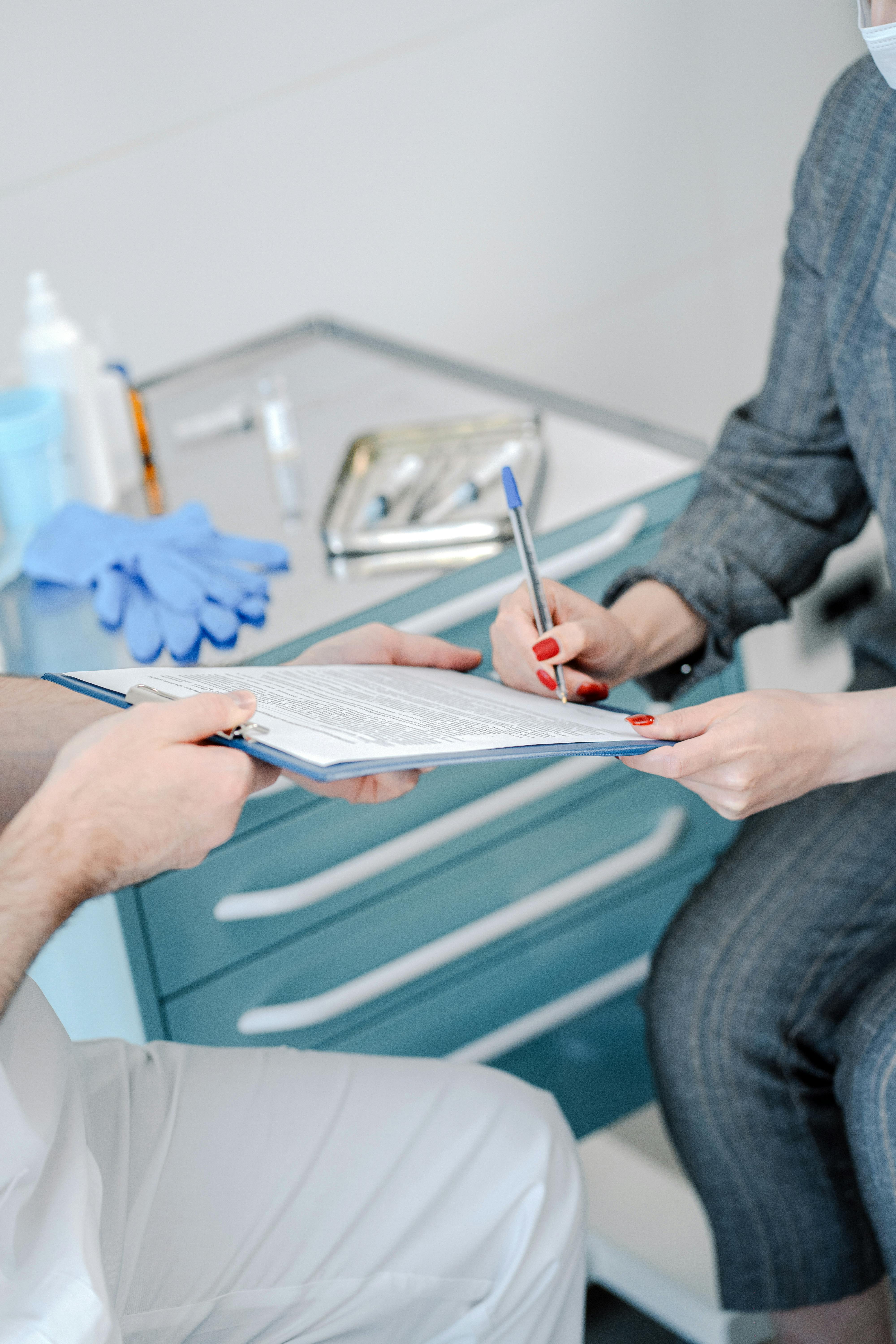 Patient signing healthcare agreement in doctor's office, focus on hands and document exchange.