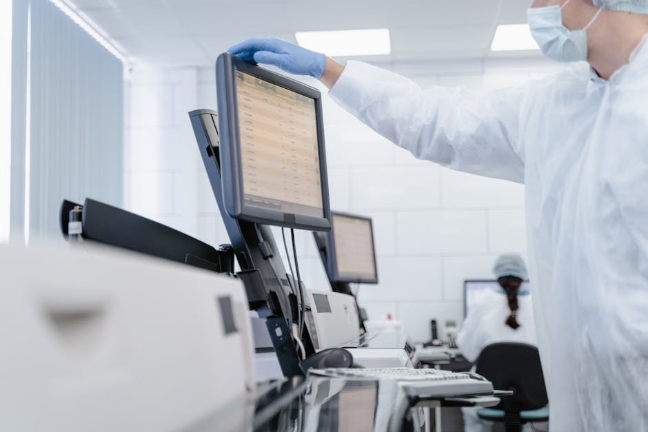 Researcher in PPE reviews data on a digital screen in a modern laboratory setting.