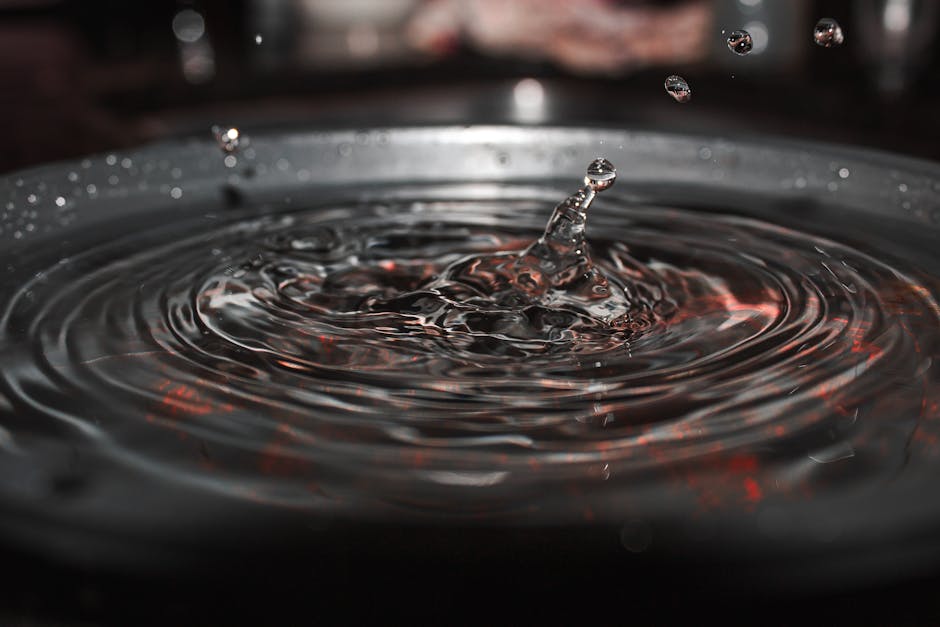 Close-up of a water droplet creating ripples in a dark, reflective surface.