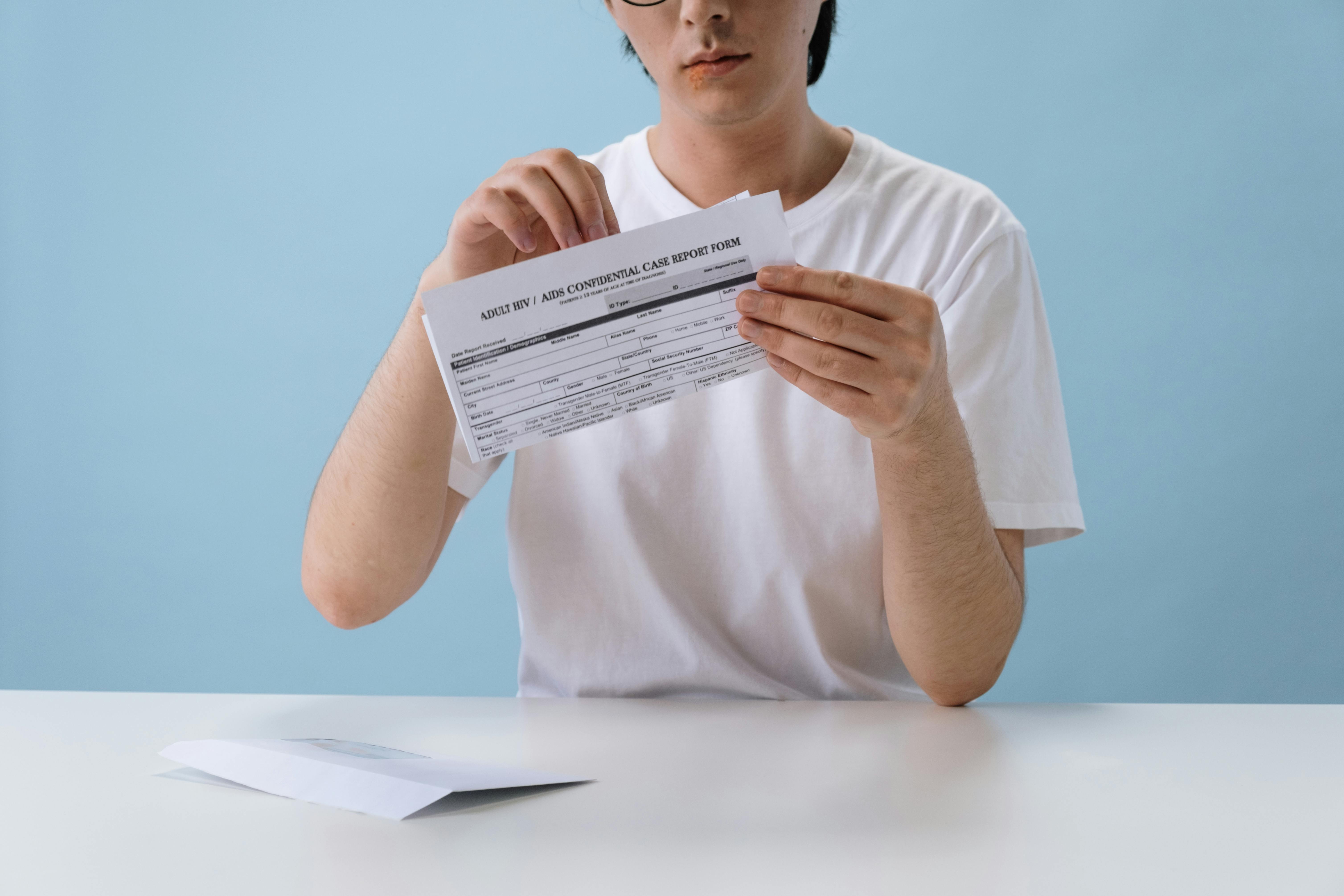 Individual reviewing a confidential HIV/AIDS case report form indoors against a blue background.