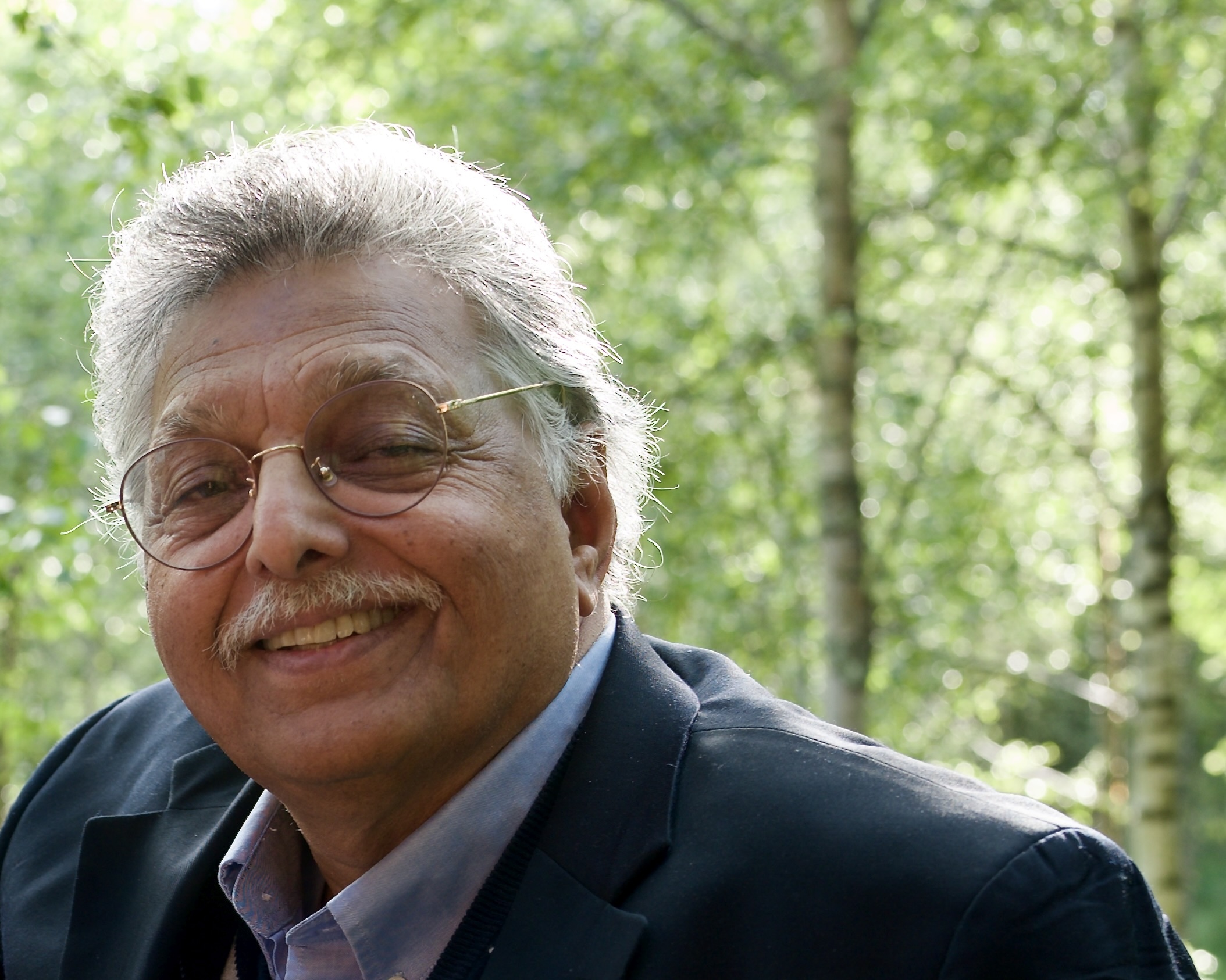 A smiling Rashad Khan in front of trees within a forest near the River Teith in Doune, Scotland.