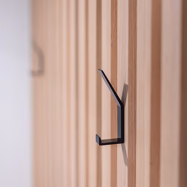 Black minimalist wall hook mounted on a vertically paneled wooden wall.