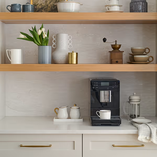Modern kitchen counter with coffee machine, white cups, a tray with cream and sugar containers, and shelves above holding cups, a coffee grinder, tulips in a vase, and decorative jars.