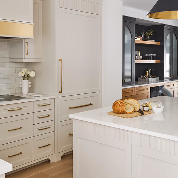 Modern kitchen with cream cabinetry, gold handles, a white island with sliced bread, and black cabinets with wooden shelves.