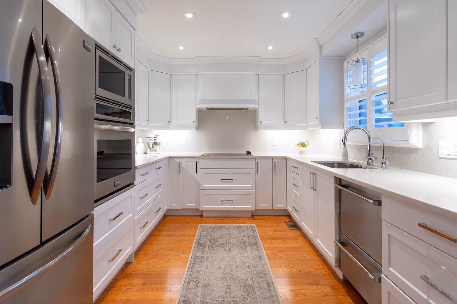 Modern kitchen with white cabinetry, stainless steel appliances, a gray patterned rug, and wooden floor.