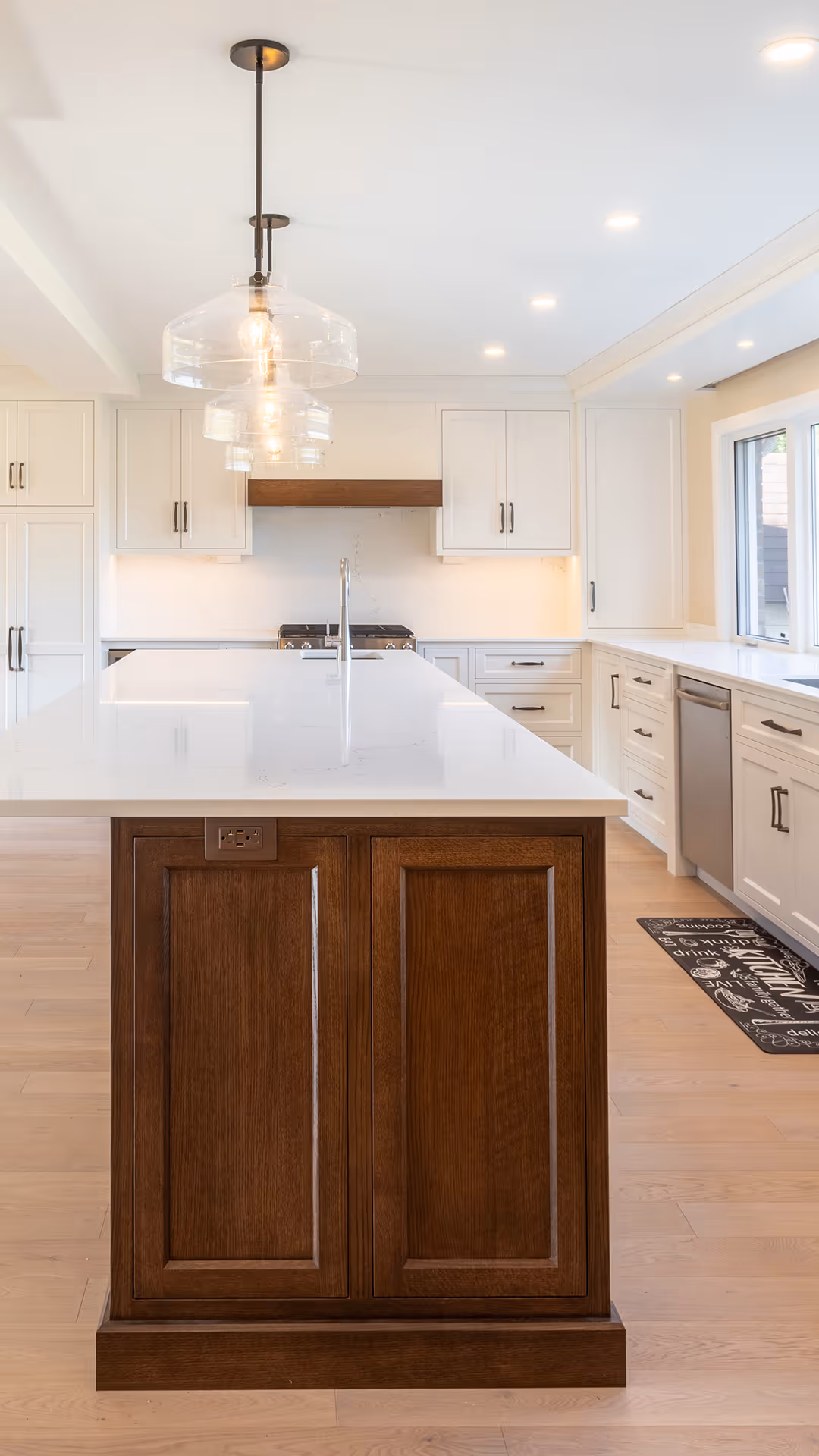 Modern kitchen corner with white cabinets, stainless steel double oven and refrigerator, hardwood floor, and a gray patterned rug.