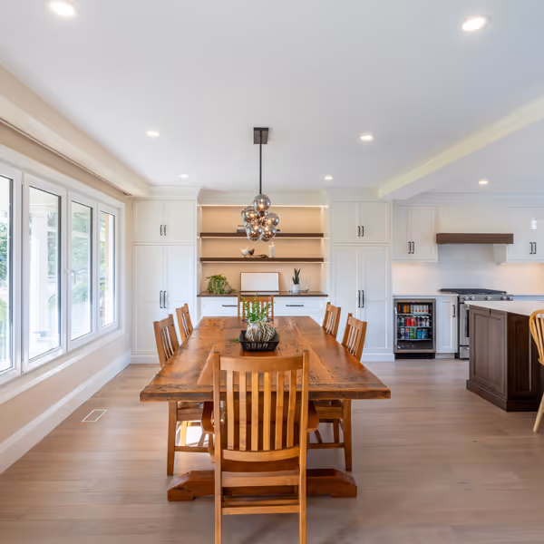 Modern dining area with a round wooden table, four light blue upholstered chairs, grey and wooden cabinetry with glass doors, open wooden shelves, and a gold geometric chandelier.