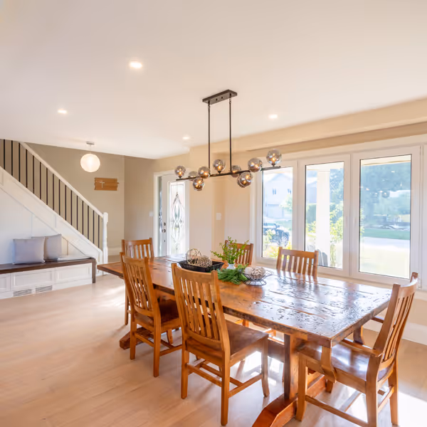 Cozy breakfast nook with curved wooden bench, white round table, black chair, and pillows by a sunlit window.